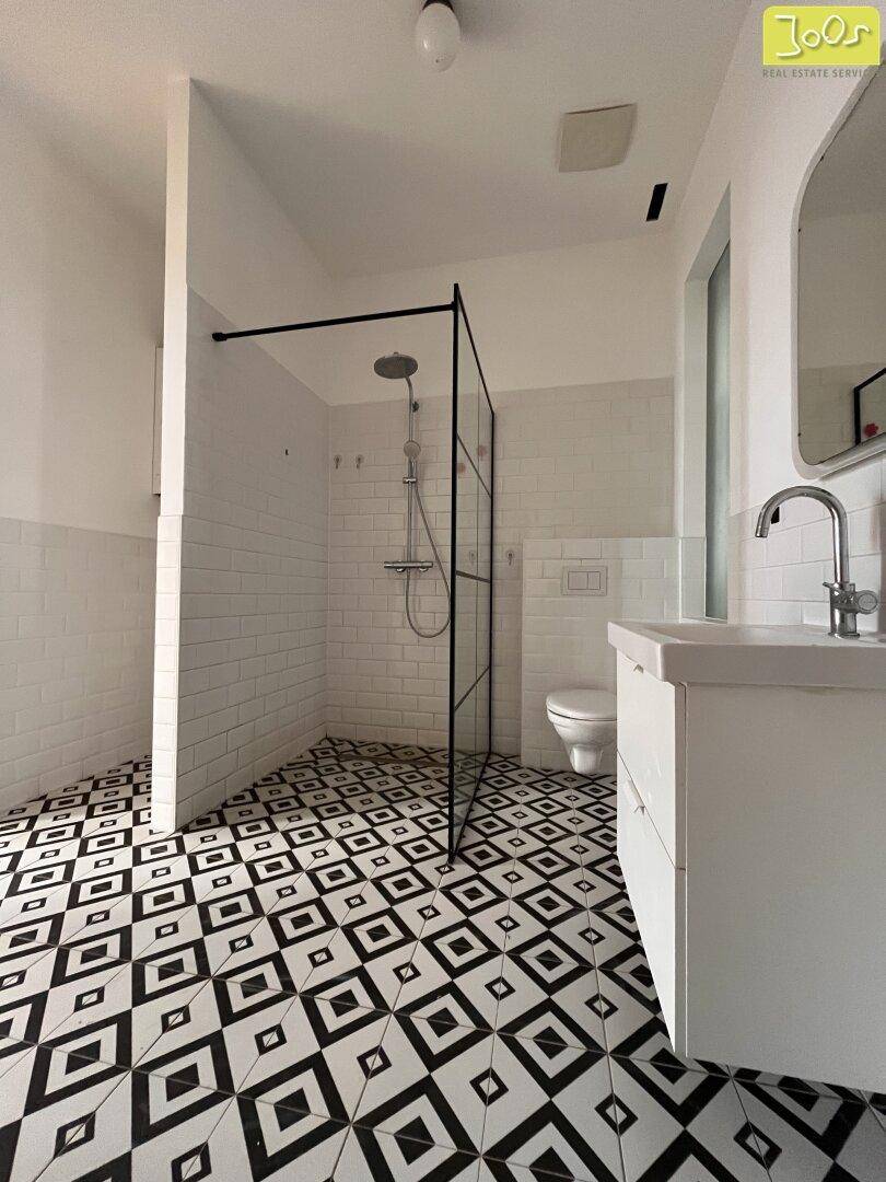 Helles Badezimmer mit großer begehbarer Dusche, Wand-WC und markantem Fliesenmuster.