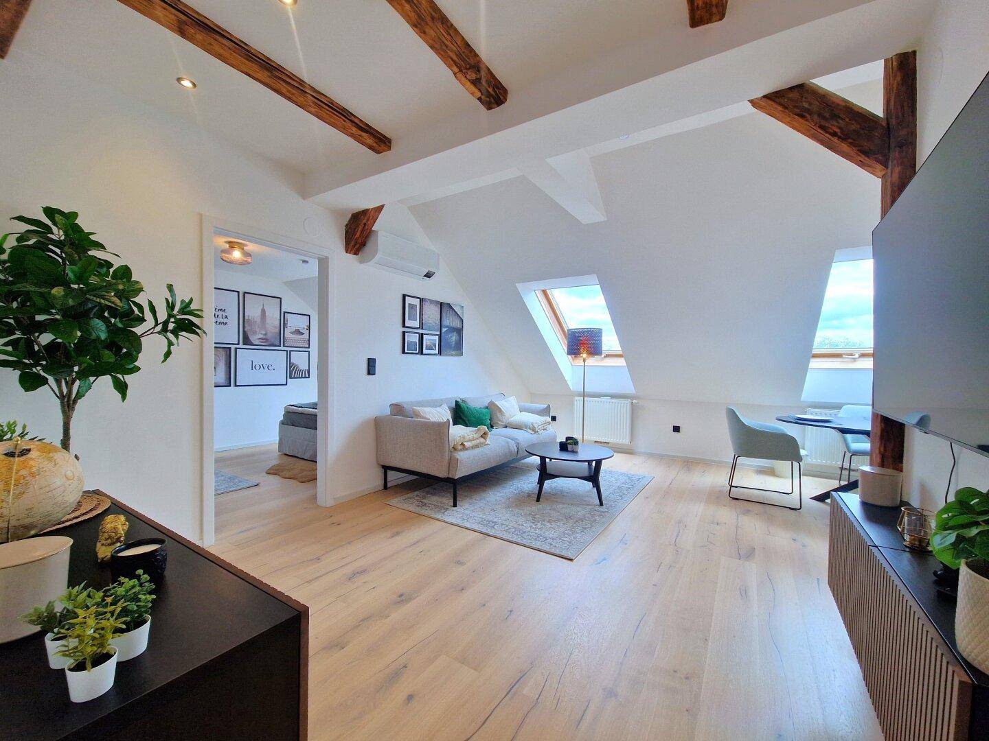 Heller Wohnbereich mit Dachschrägen, Holzbalken, modernem Sofa und Blick auf die Dachfenster.
