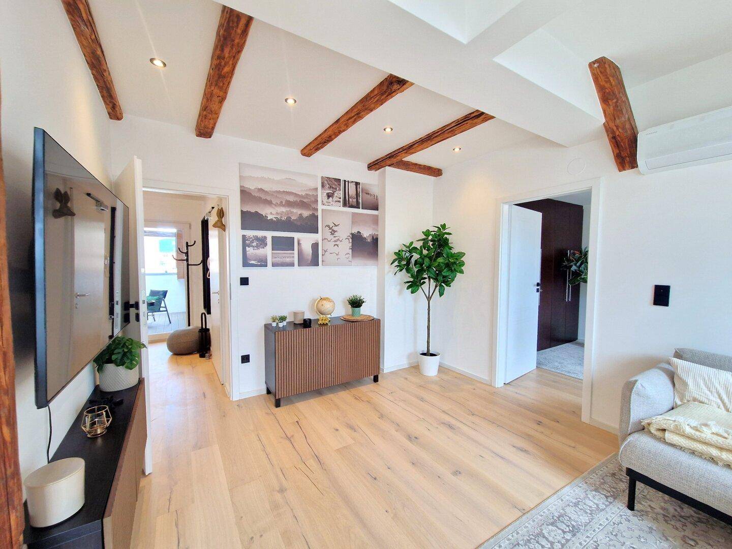 Geräumiger Wohnbereich mit Holzbalken, moderner Einrichtung und Zugang zum Eingangsbereich und zur Terrasse.
