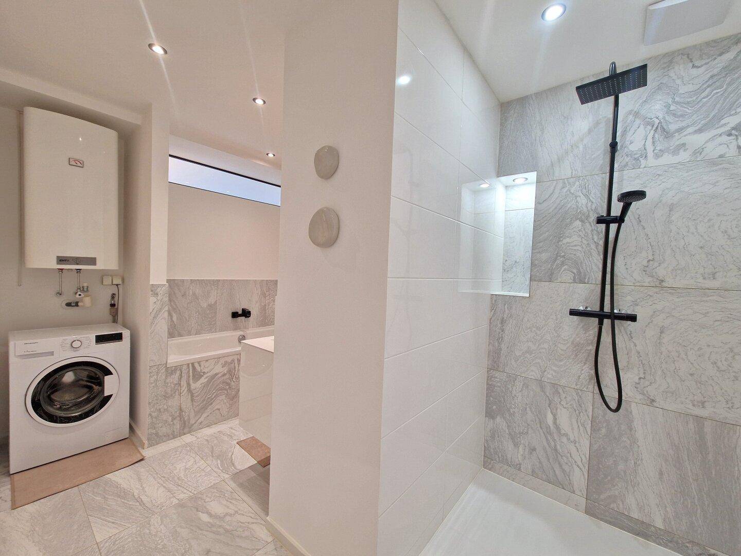 Helles Badezimmer mit begehbarer Dusche, Waschmaschine und modernen Fliesen.