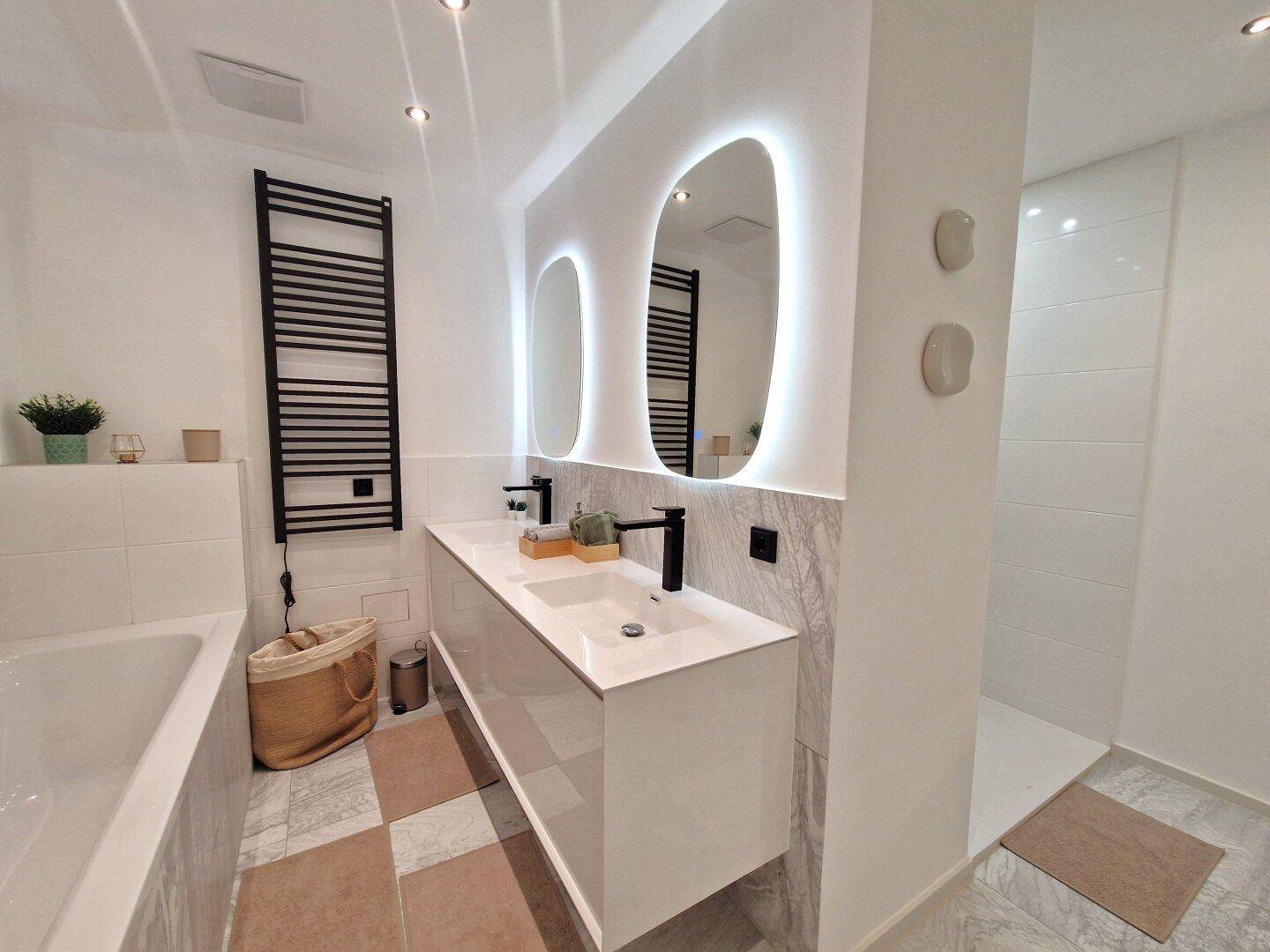 Modernes Badezimmer mit Doppelwaschbecken, beleuchteten Spiegeln, Badewanne und begehbarer Dusche.