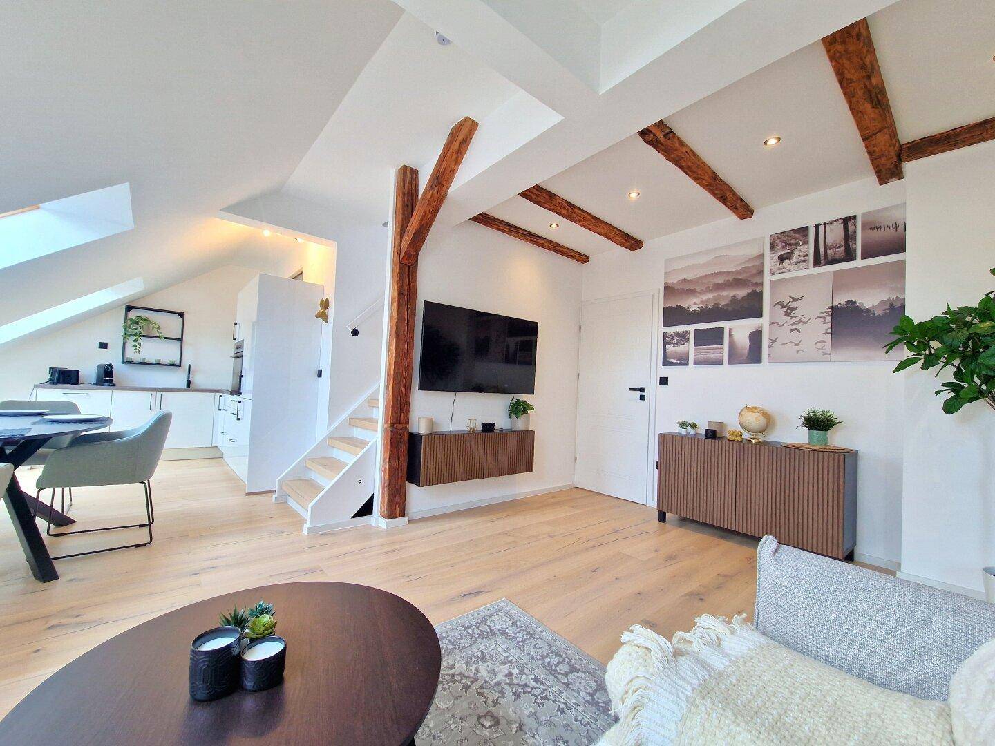 Offener Wohnbereich mit Holzbalken, modernem Sofa und Esstisch, der zum Entspannen einlädt.