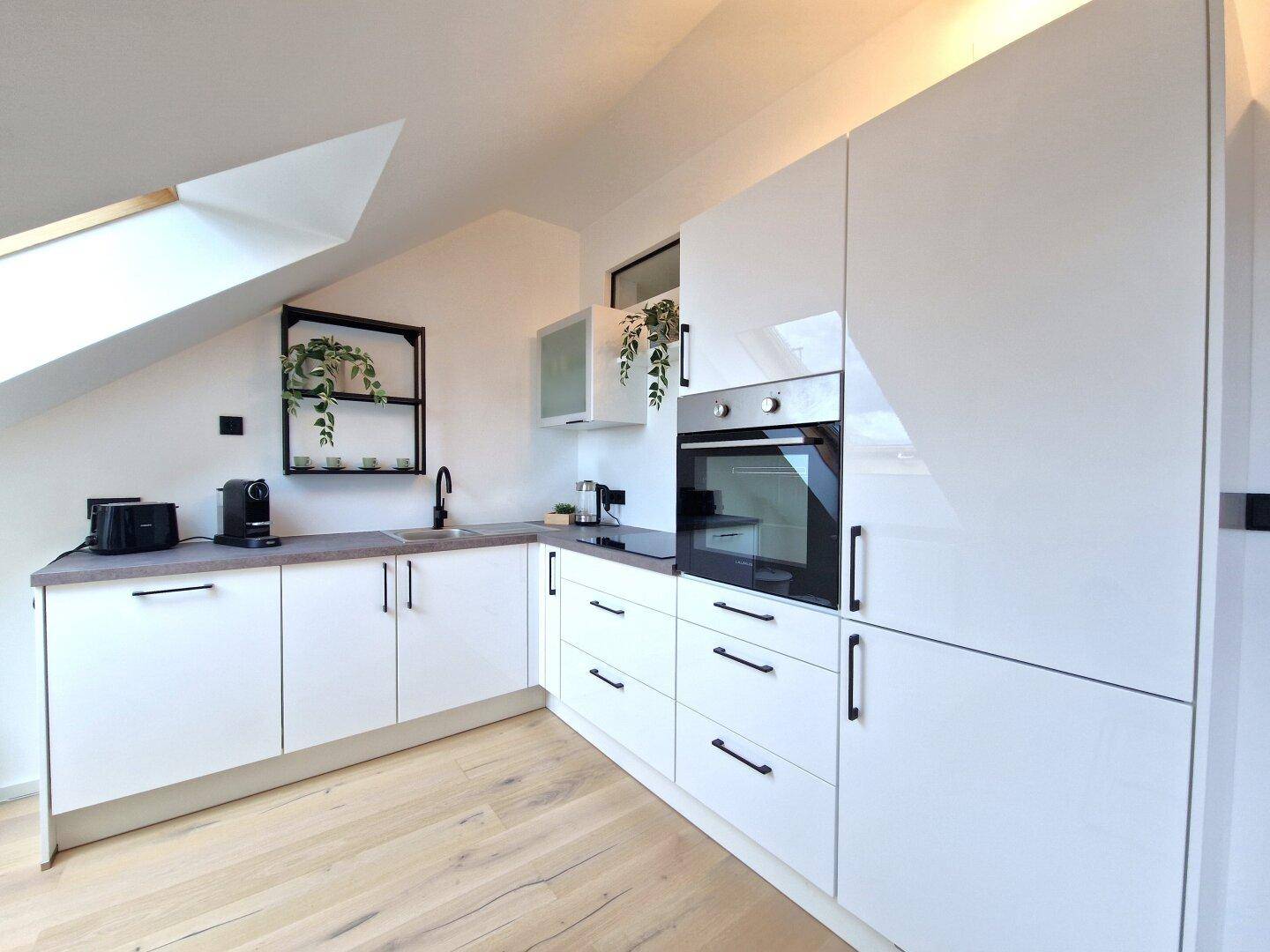 Helle, moderne Küche mit weißen Hochglanzschränken, integriertem Backofen und Dachfenster.