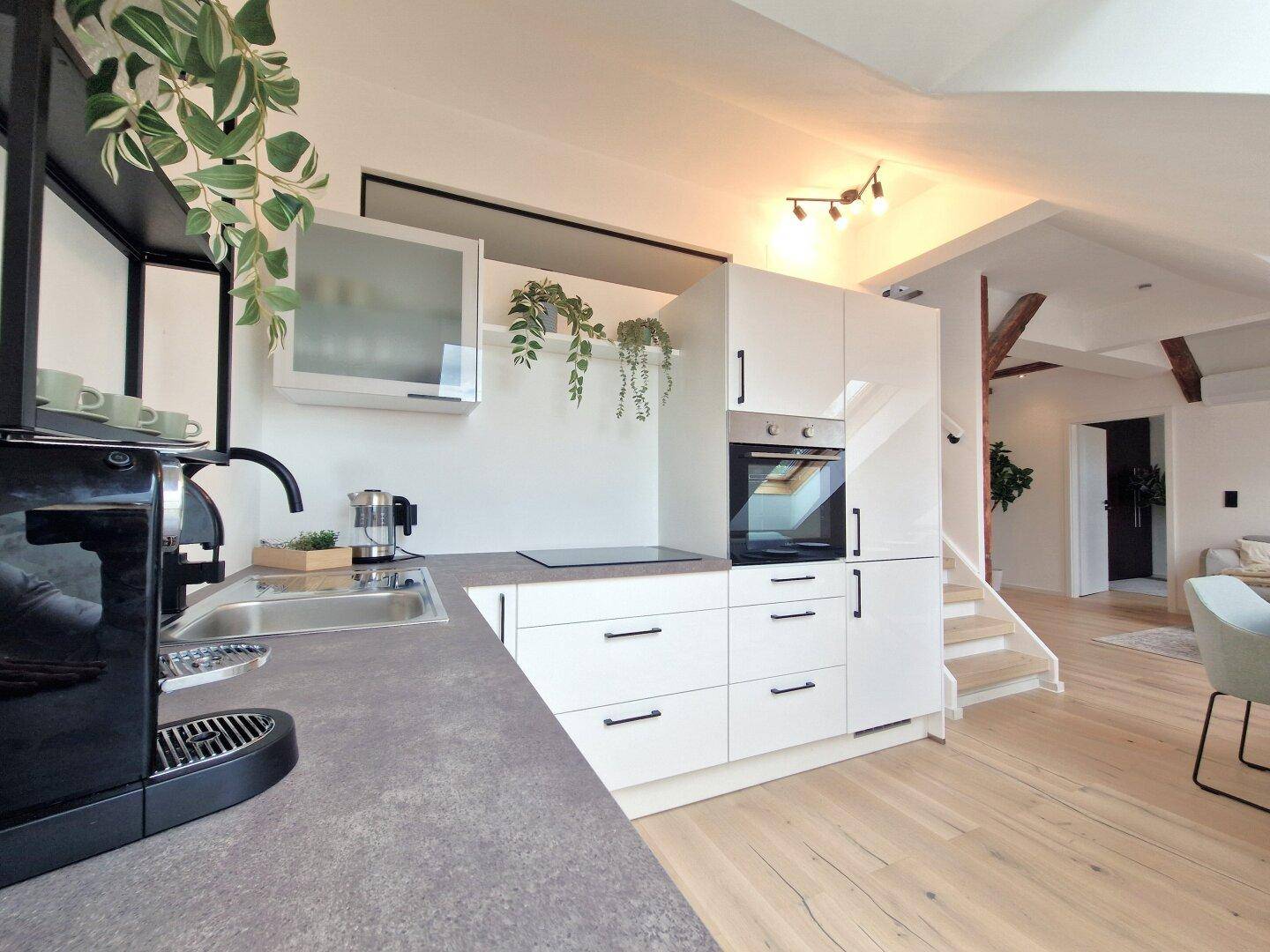 Moderne Einbauküche mit weißen Hochglanzfronten, integrierten Geräten und Arbeitsplatte in Steinoptik.