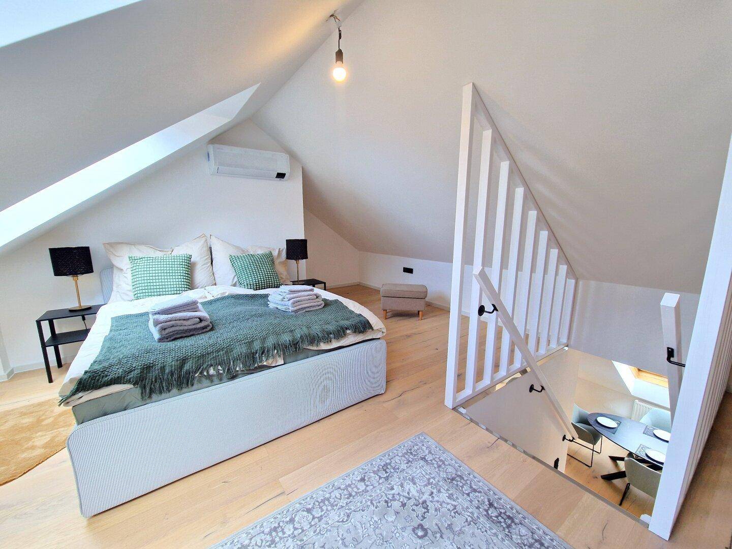 Schlafzimmer im Dachgeschoss mit Doppelbett, Dachschräge und Blick auf die untere Wohnebene.