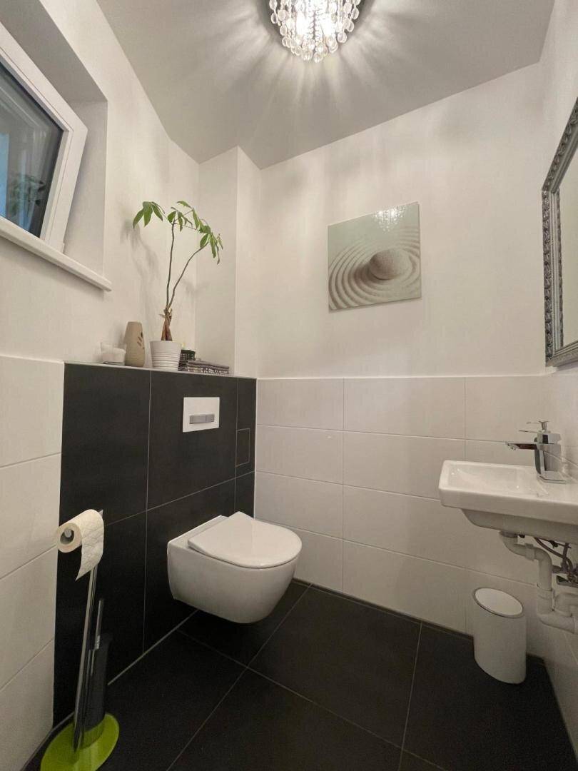 Gäste-WC mit wandhängendem WC, kleinem Waschbecken und modernen Fliesen.