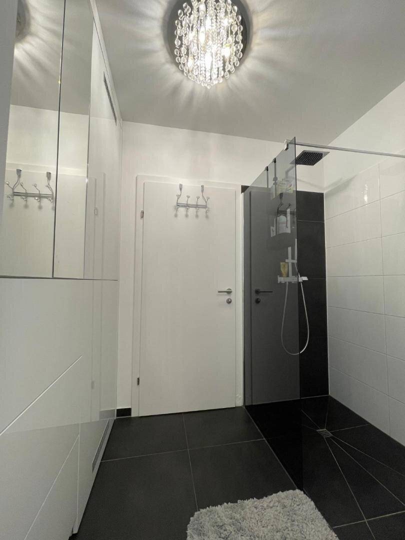 Elegantes Badezimmer mit ebenerdiger Dusche, dunklen Fliesen und minimalistischem Design.