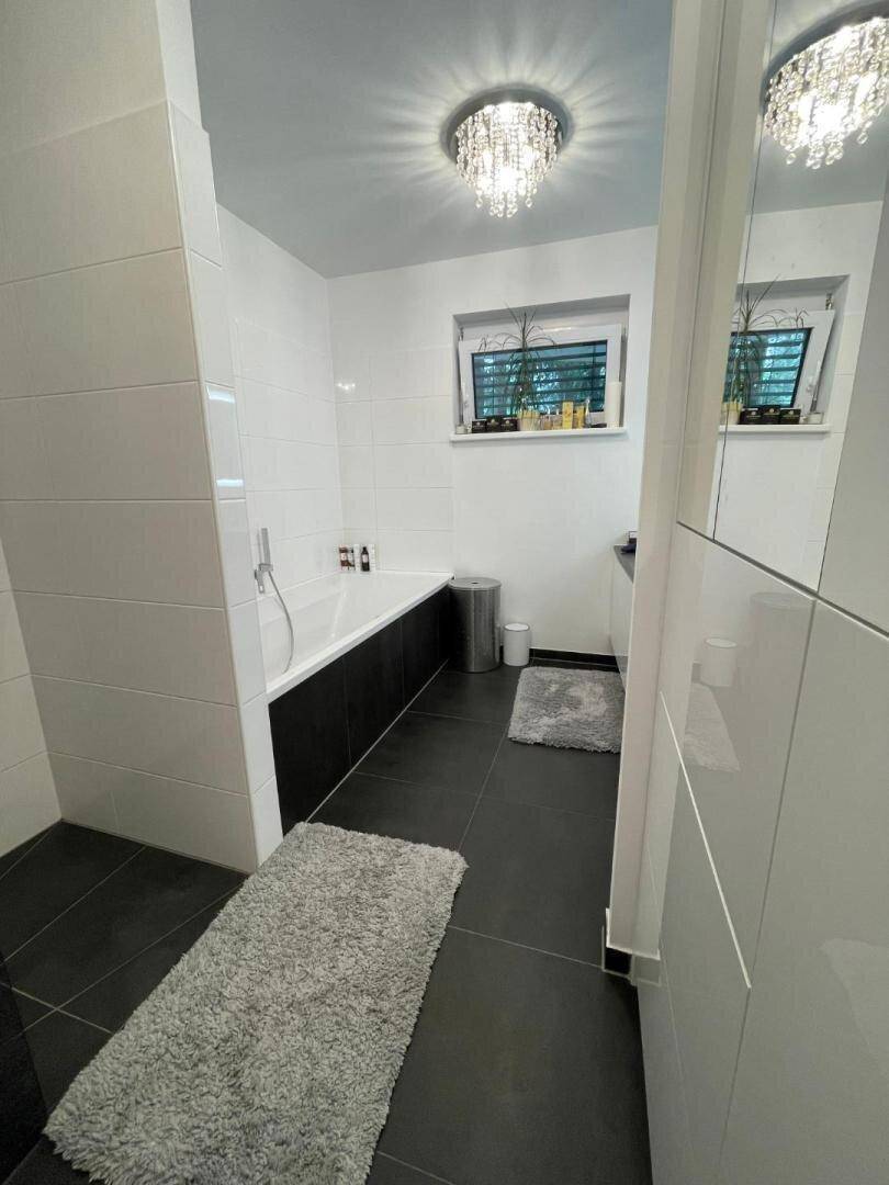 Modernes Badezimmer mit Badewanne, dunklen Bodenfliesen und weißen Wandfliesen.