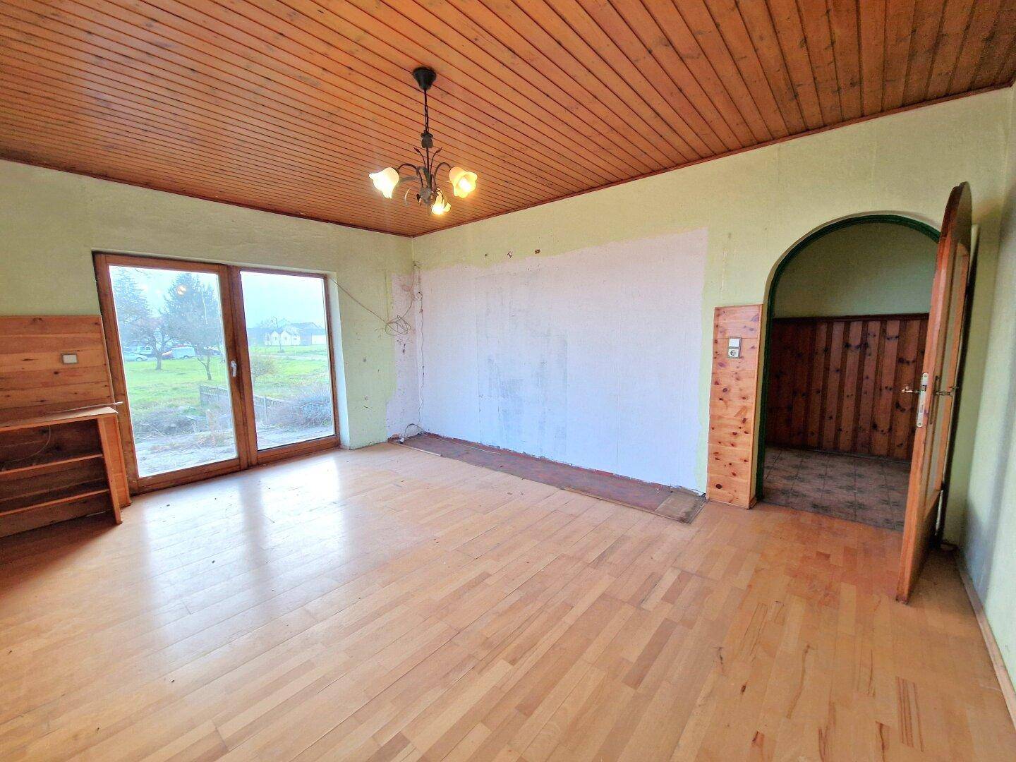 Zimmer mit Holzbalkendecke und Parkettboden, das auf eine Modernisierung wartet und viel Potenzial bietet.