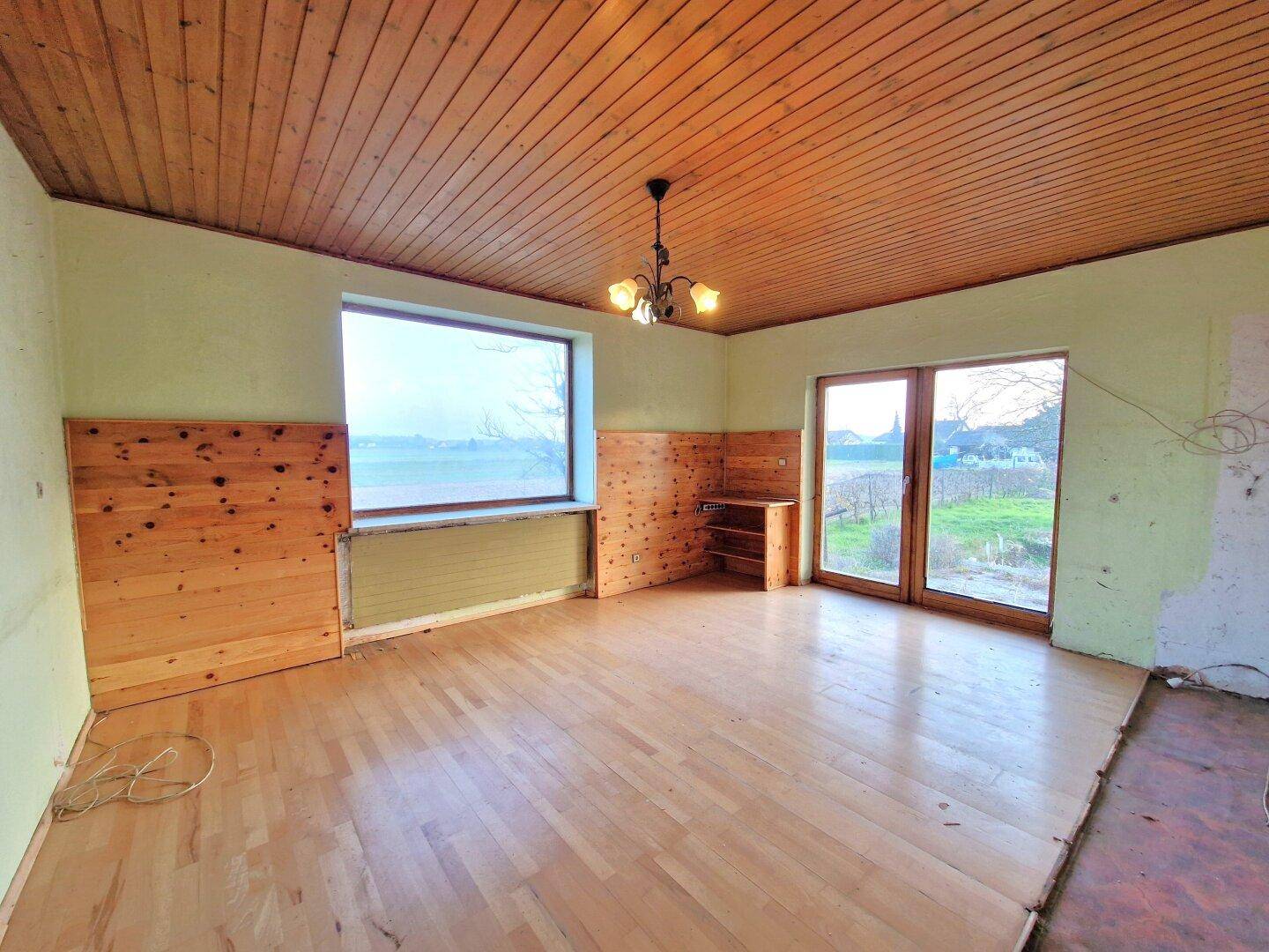 Geräumiges Zimmer mit Holzbalkendecke, Parkettboden und Zugang zu einem Balkon oder Garten.