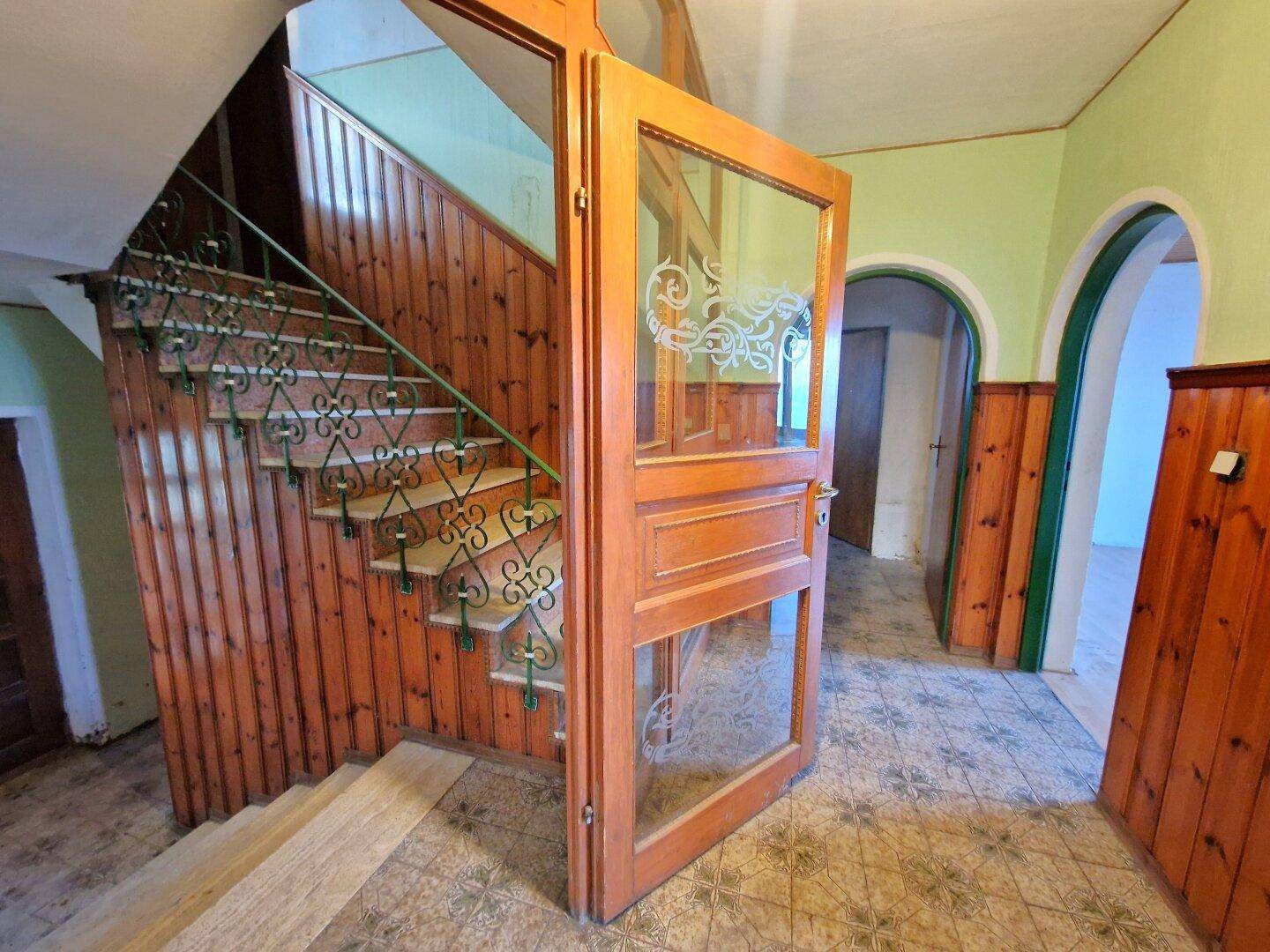 Treppenhaus mit Holzstufen, schmiedeeisernem Geländer und Holzvertäfelung, die zum Obergeschoss führt.