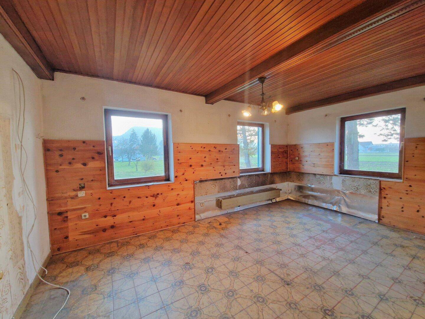 Großer Raum mit Holzbalkendecke, gemusterten Fliesen und mehreren Fenstern für viel Tageslicht.