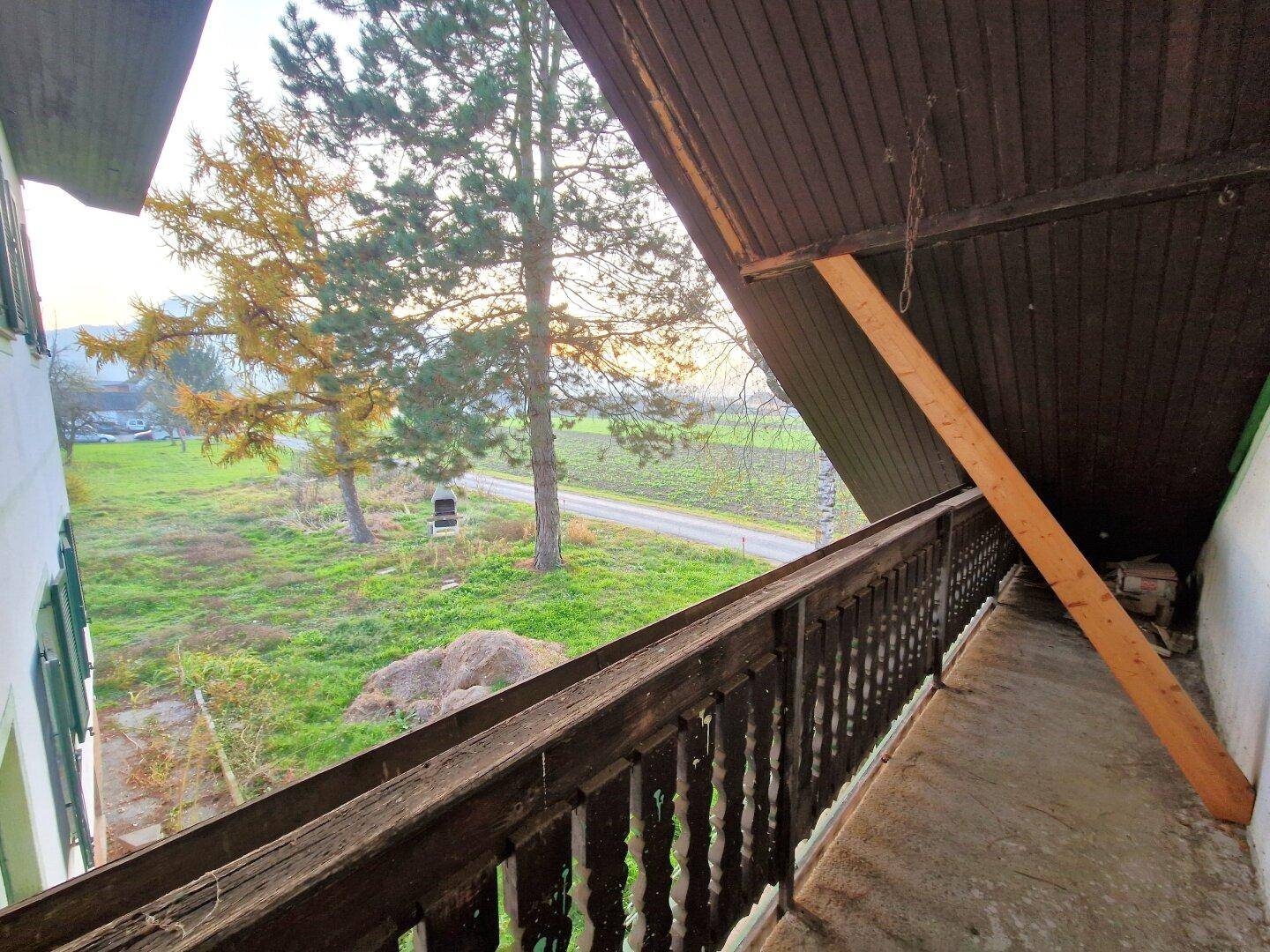 Alter Holzbalkon mit Blick auf die ländliche Umgebung und Bäume, der eine Renovierung benötigt.