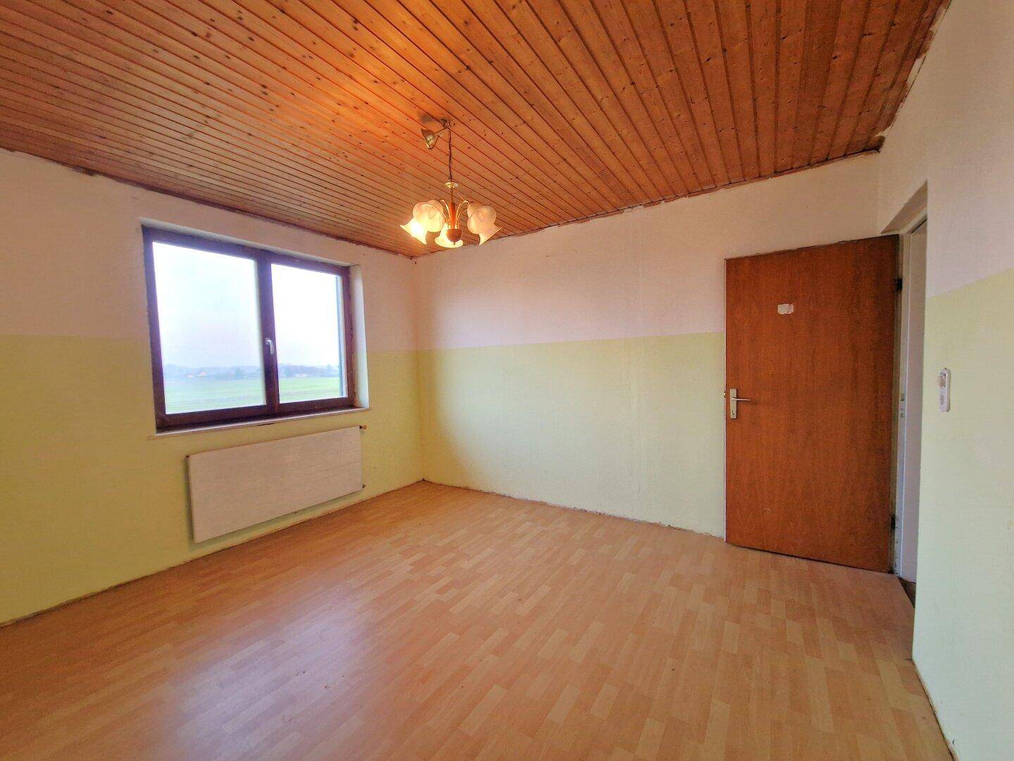 Zimmer mit Holzbalkendecke, Parkettboden und Fenster, das auf eine Renovierung wartet.