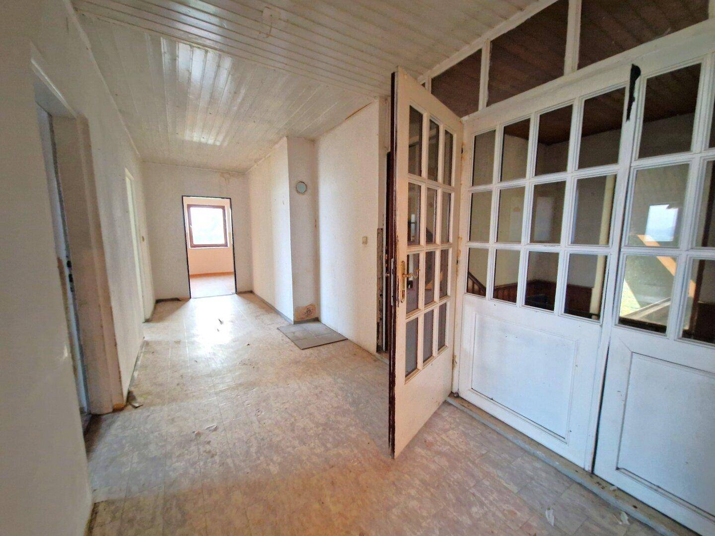 Heller Flur mit weißer Holzdecke und alten Türen, der auf eine Modernisierung wartet.