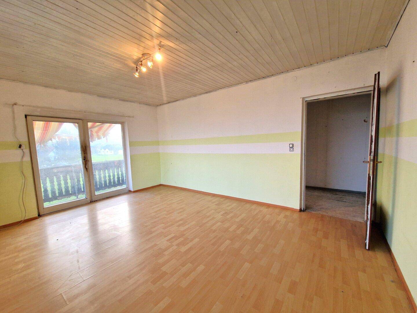 Helles Zimmer mit Holzboden und Zugang zu einem Balkon, bereit zur individuellen Gestaltung.