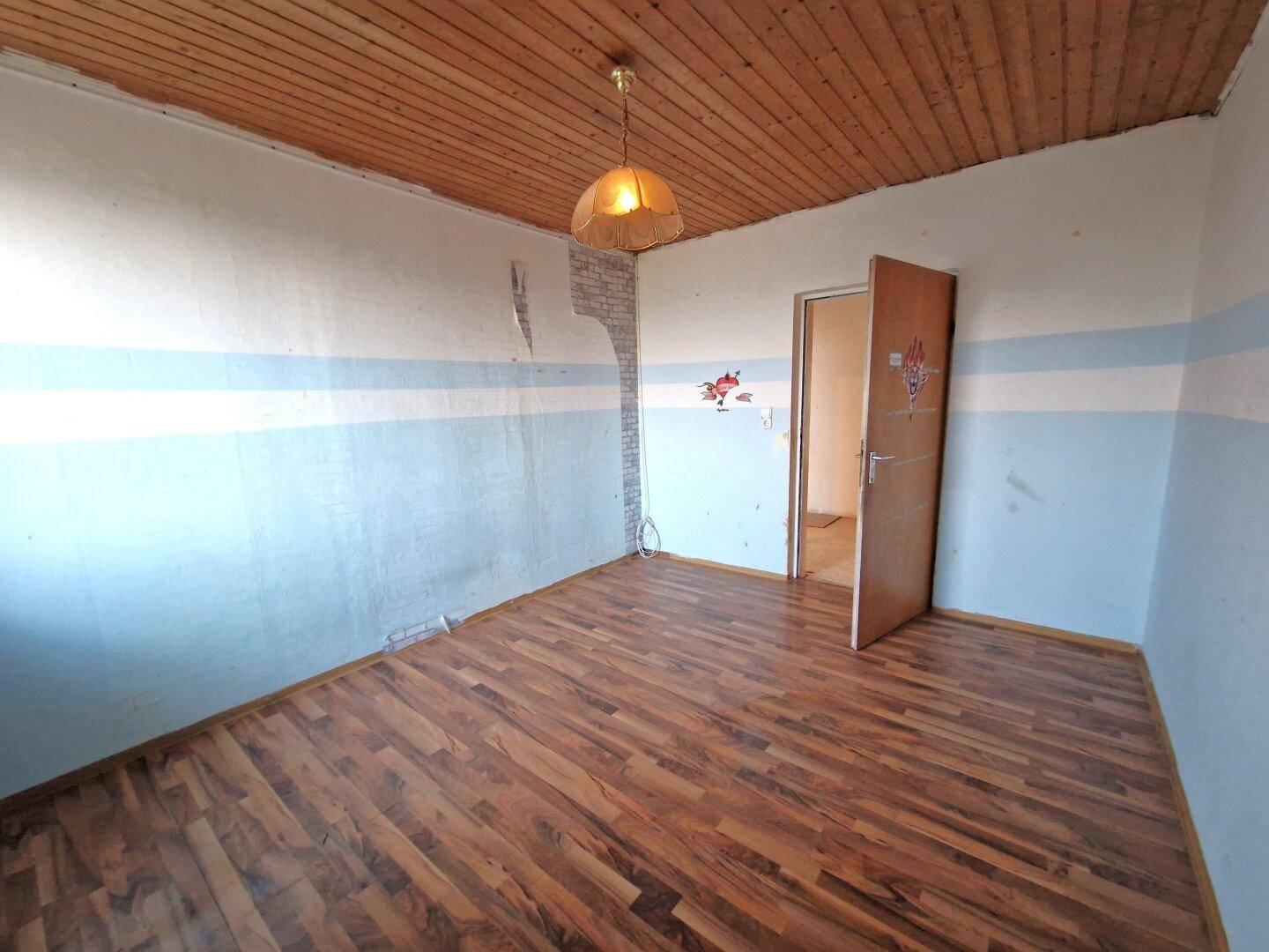 Zimmer mit Holzbalkendecke und Holzboden, das eine Renovierung benötigt und viel Potenzial bietet.