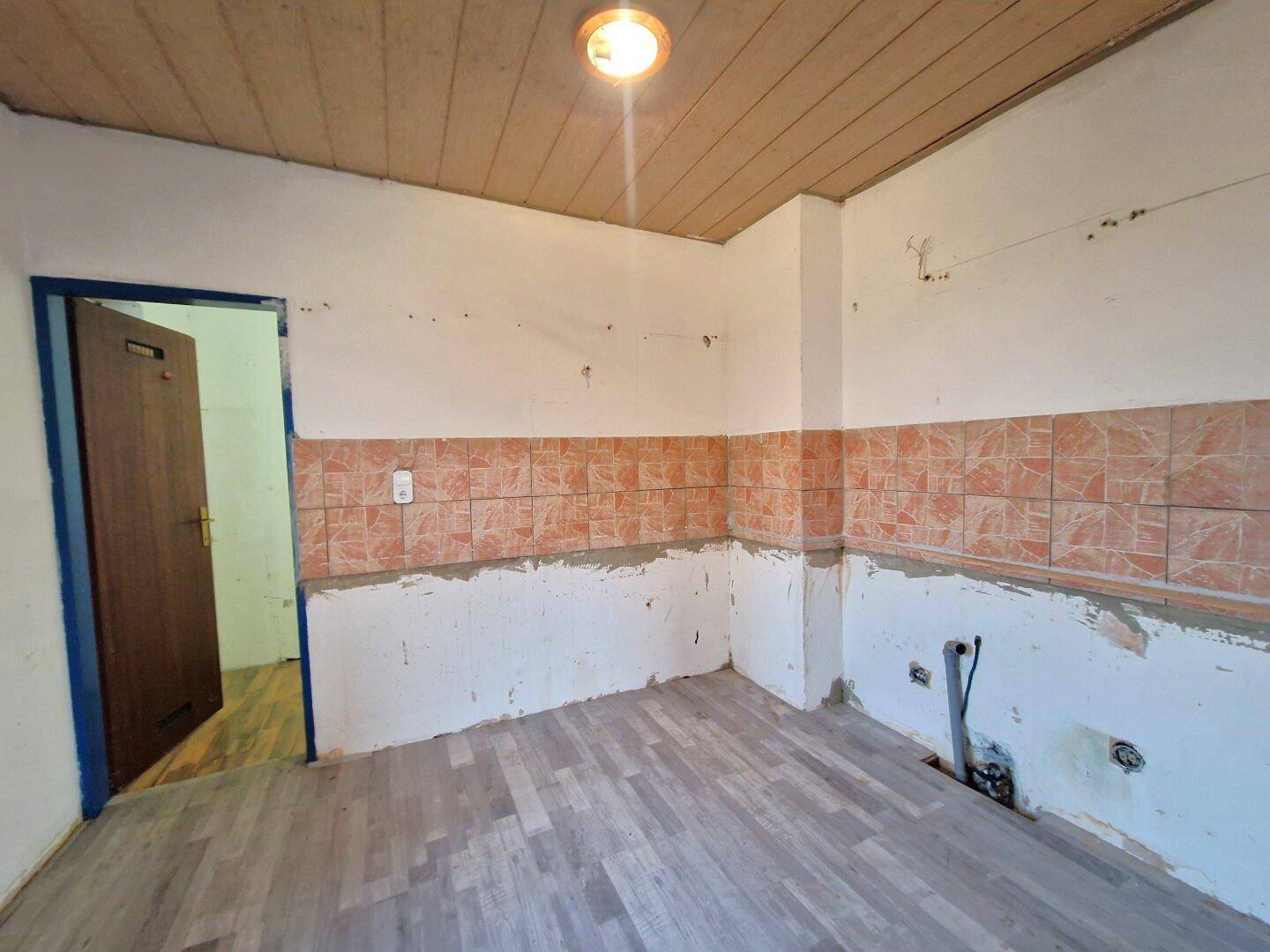 Leere Küche mit gefliestem Spritzschutz und Holzboden, bereit für eine neue Einrichtung.