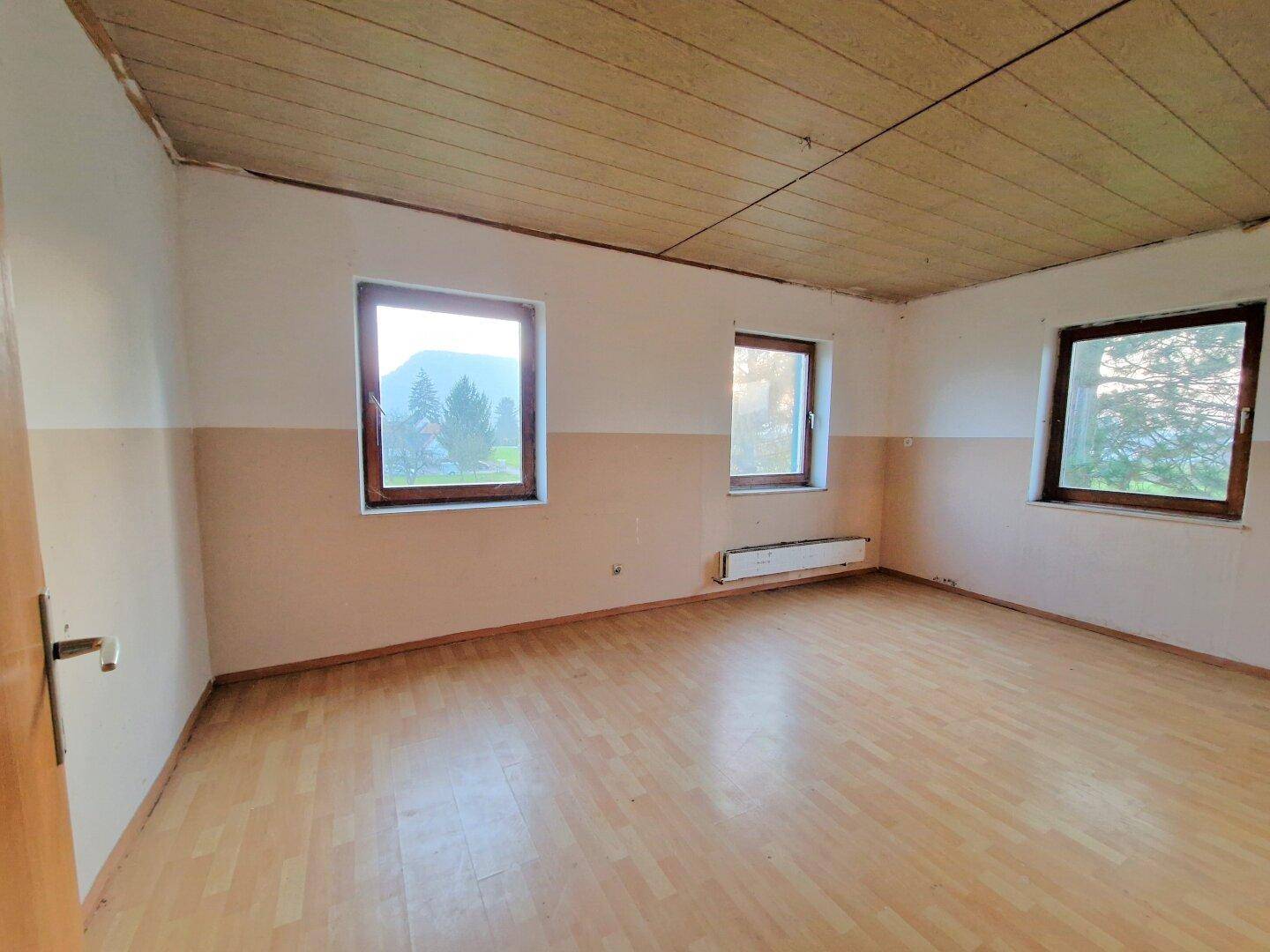 Geräumiges Zimmer mit mehreren Fenstern und Holzboden, bietet viel natürliches Licht.