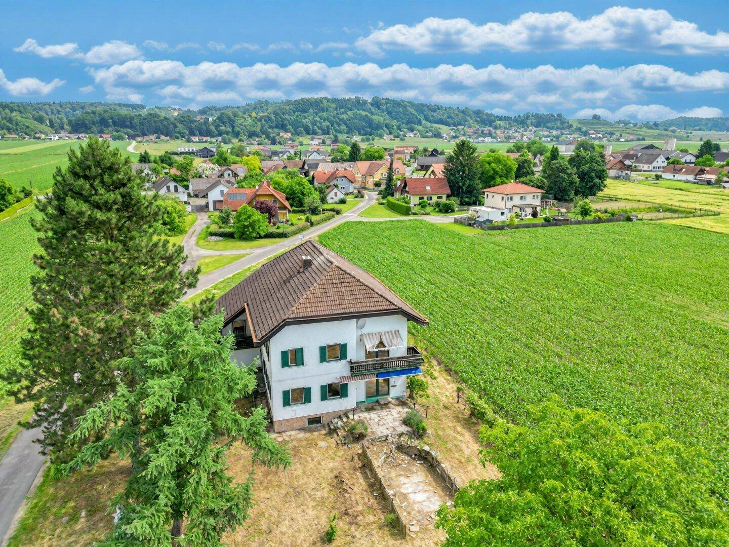 Luftaufnahme eines Hauses in ländlicher Umgebung, umgeben von grünen Feldern und Bäumen.
