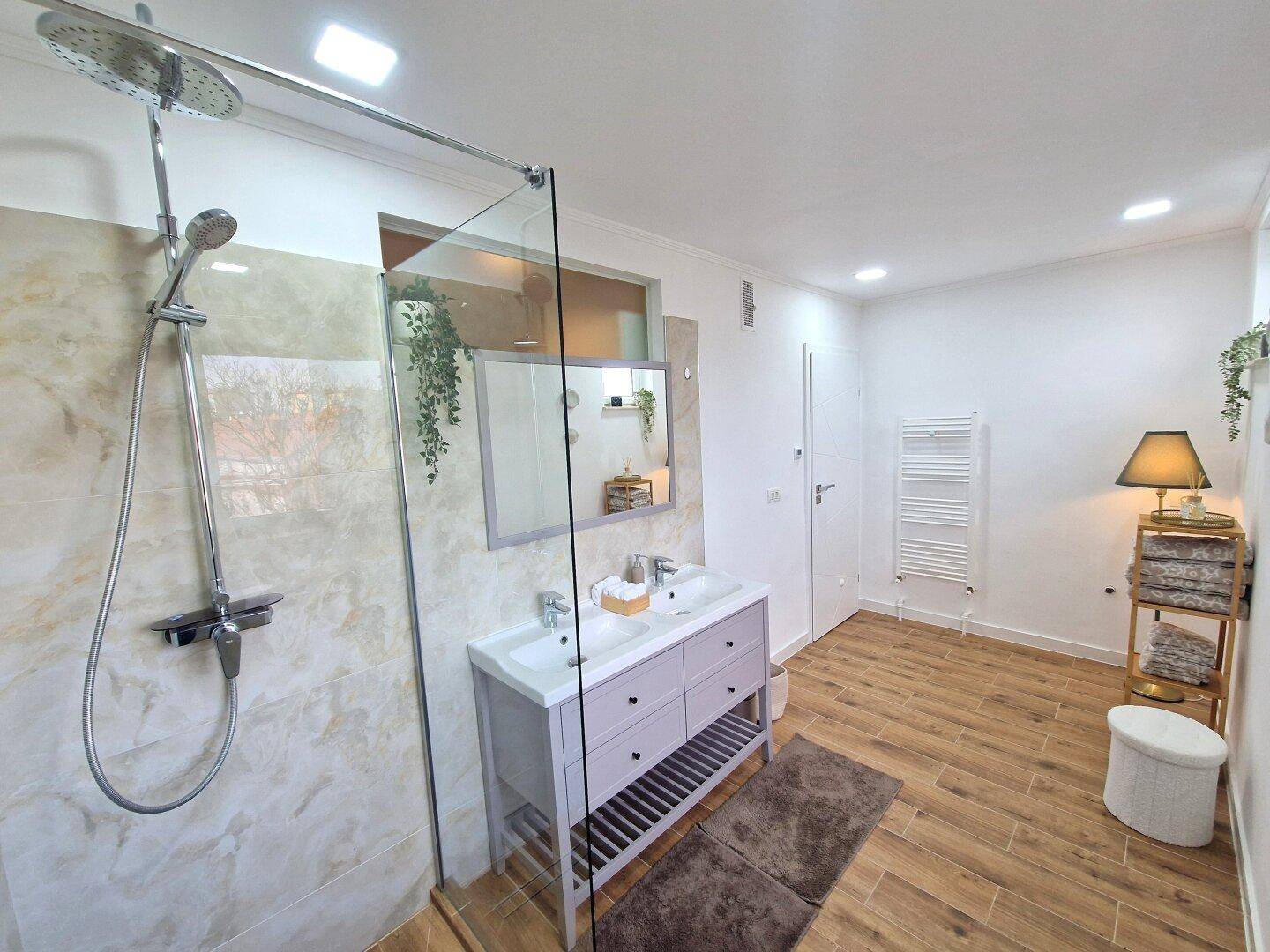 Modernes Badezimmer mit Doppelwaschbecken, großer begehbarer Dusche und Holzoptikfliesen.
