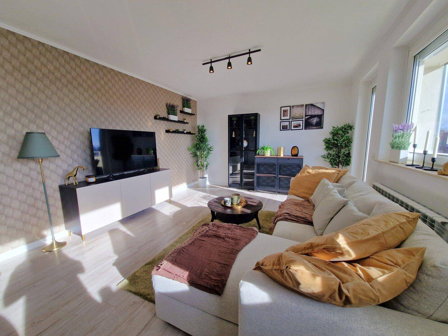 Helles Wohnzimmer mit bequemer Couch, TV-Möbel und dekorativer Wandtapete.