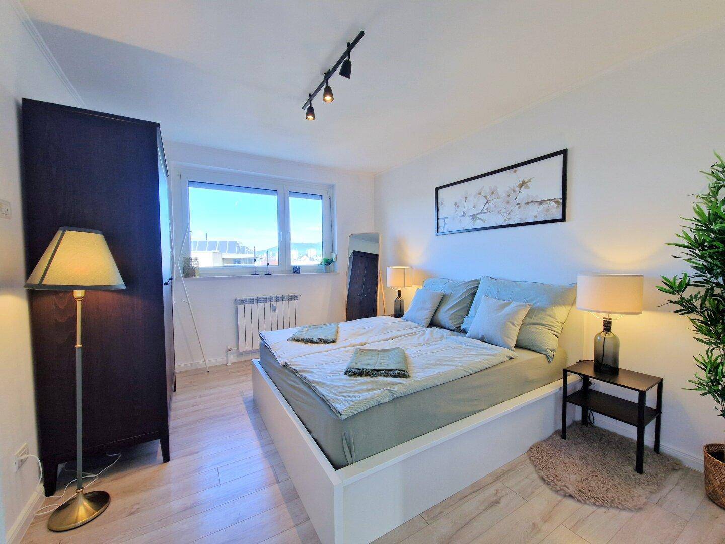 Helles Schlafzimmer mit Doppelbett, großem Fenster und modernem Interieur.