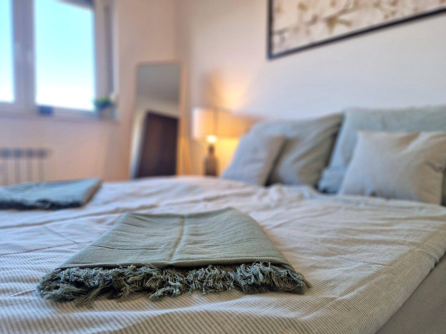 Nahaufnahme des Bettes mit Kissen und Decke in einem hellen Schlafzimmer.