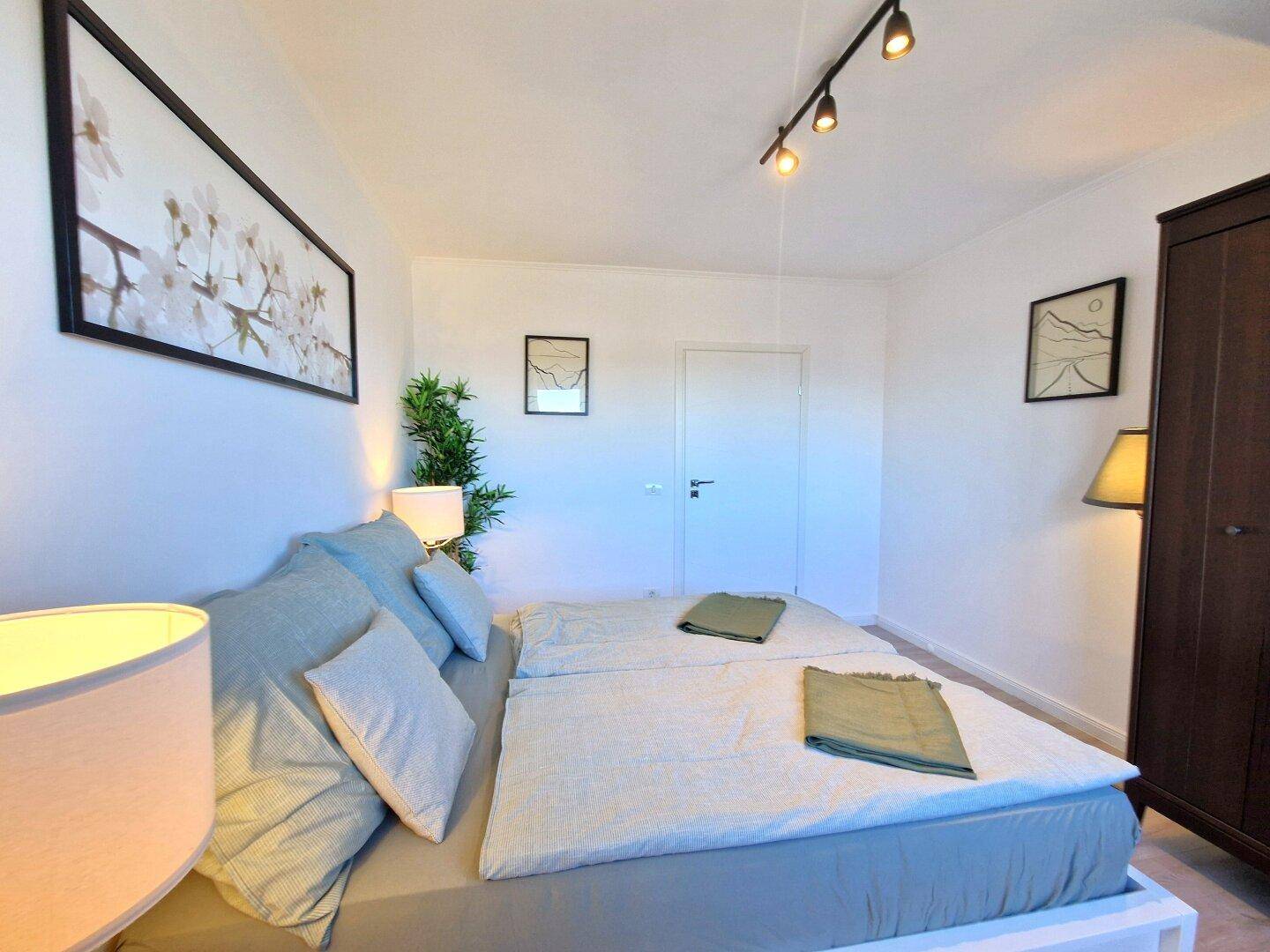 Schlafzimmer mit Doppelbett, Kleiderschrank und moderner Beleuchtung.