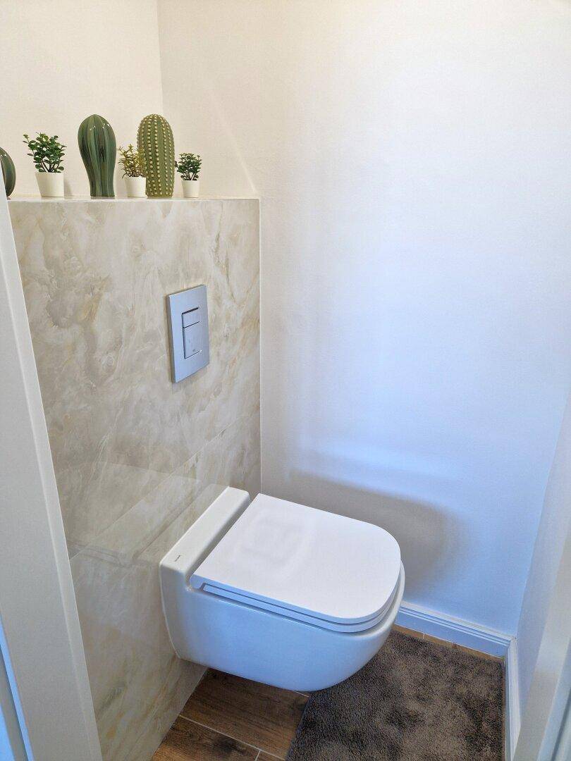 Modernes Gäste-WC mit wandhängender Toilette und dekorativen Pflanzen.