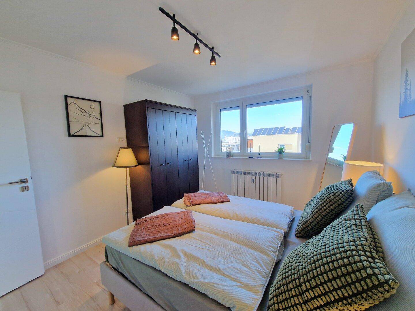 Helles Schlafzimmer mit Doppelbett, Kleiderschrank und Blick auf die Umgebung mit Solaranlagen.