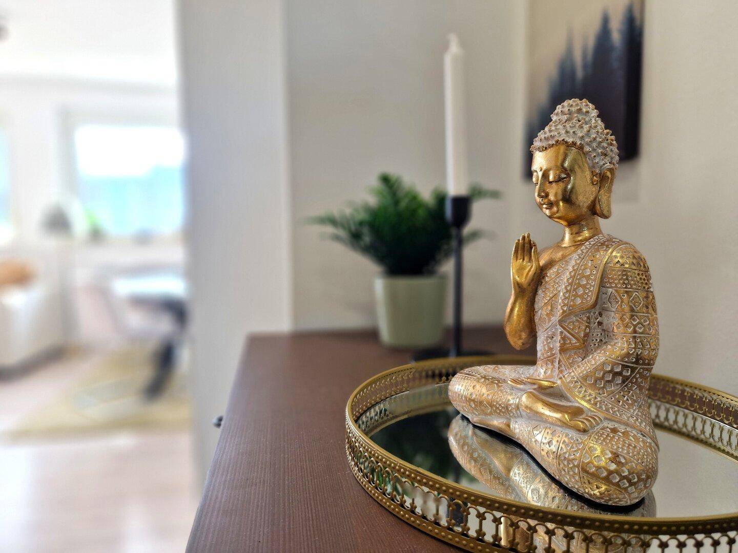 Dekorative goldene Buddha-Statue auf einem Spiegel-Tablett als stilvolles Detail.
