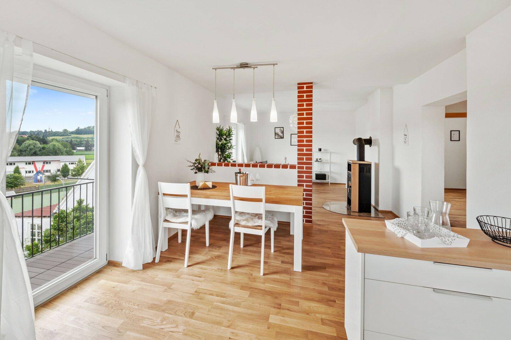 Heller Essbereich mit Holztisch, Parkettboden und Zugang zu einem Balkon mit Weitblick.