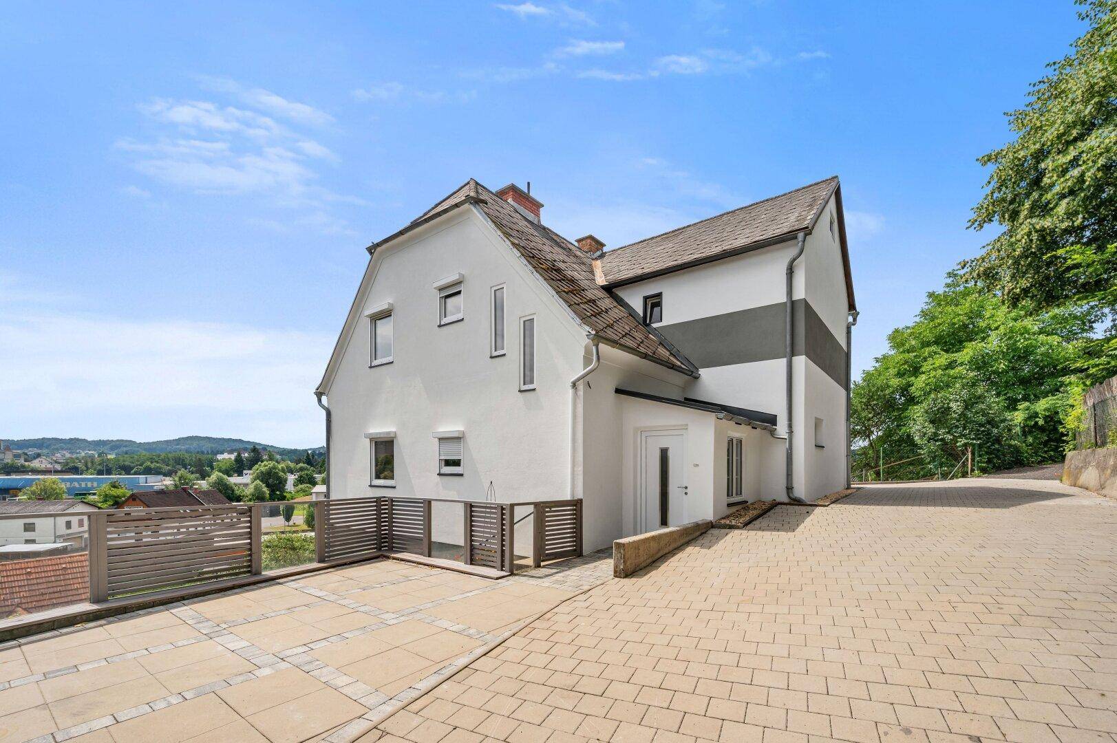 Ansicht des Hauses von der Auffahrt mit gepflastertem Bereich und moderner Architektur.