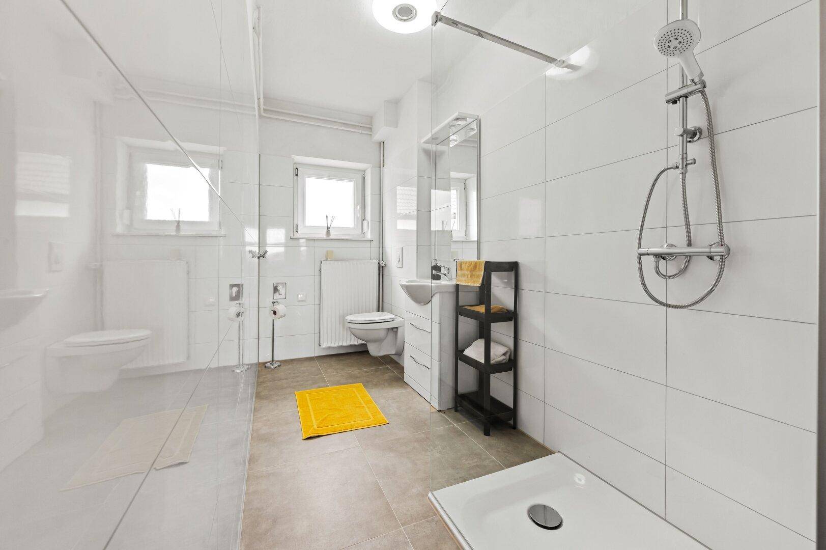 Modernes Badezimmer mit großer Dusche, weißen Fliesen und Fenster für Tageslicht.