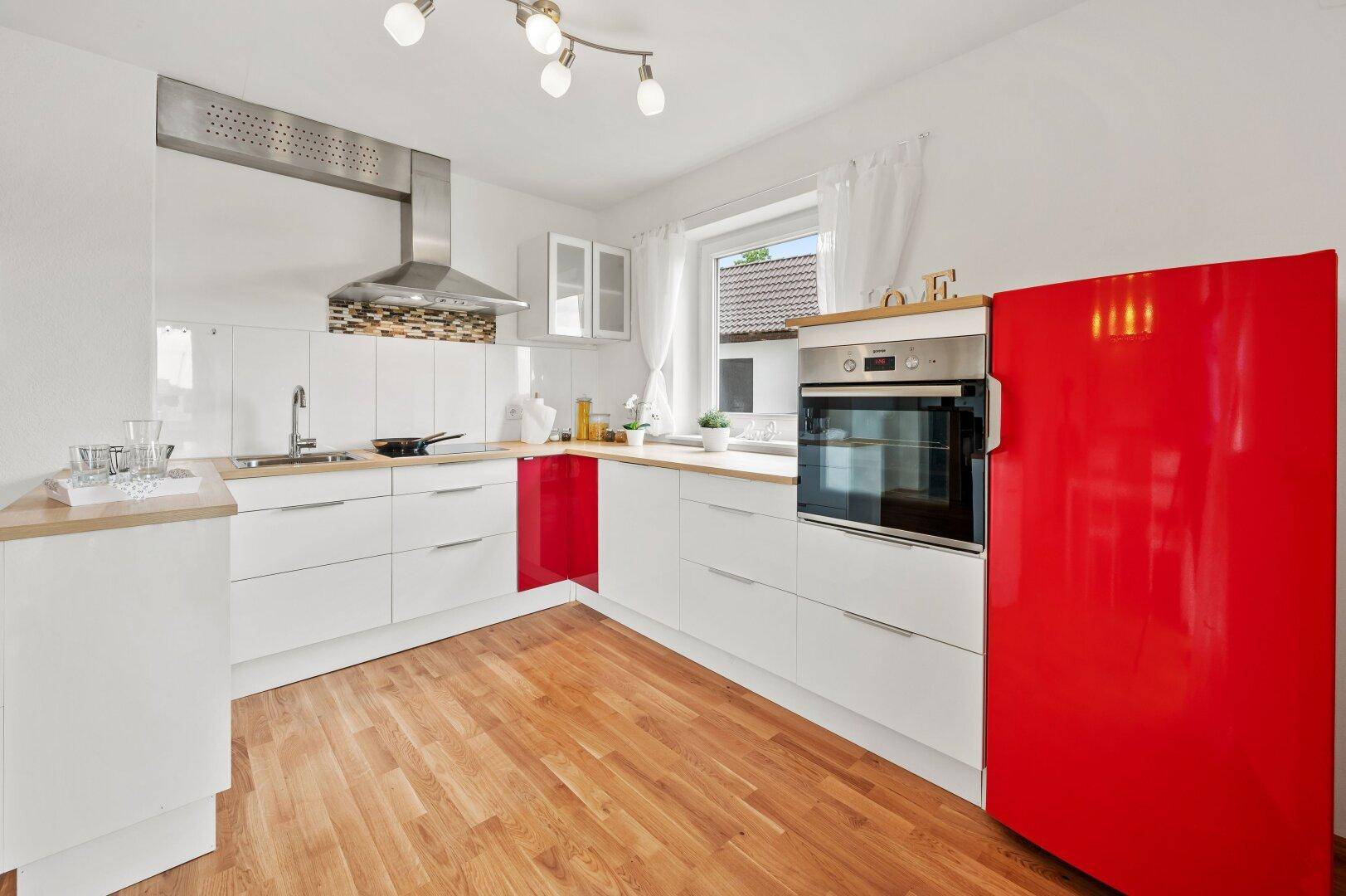 Moderne Küche mit weißen Hochglanzfronten, Holzarbeitsplatte und auffälligem rotem Kühlschrank.