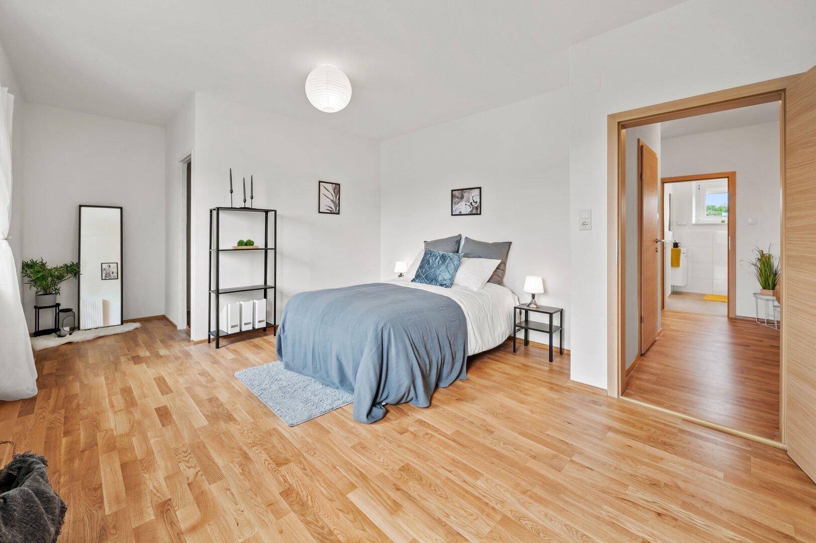 Geräumiges Schlafzimmer mit Holzboden und direktem Zugang zu einem modernen Badezimmer.