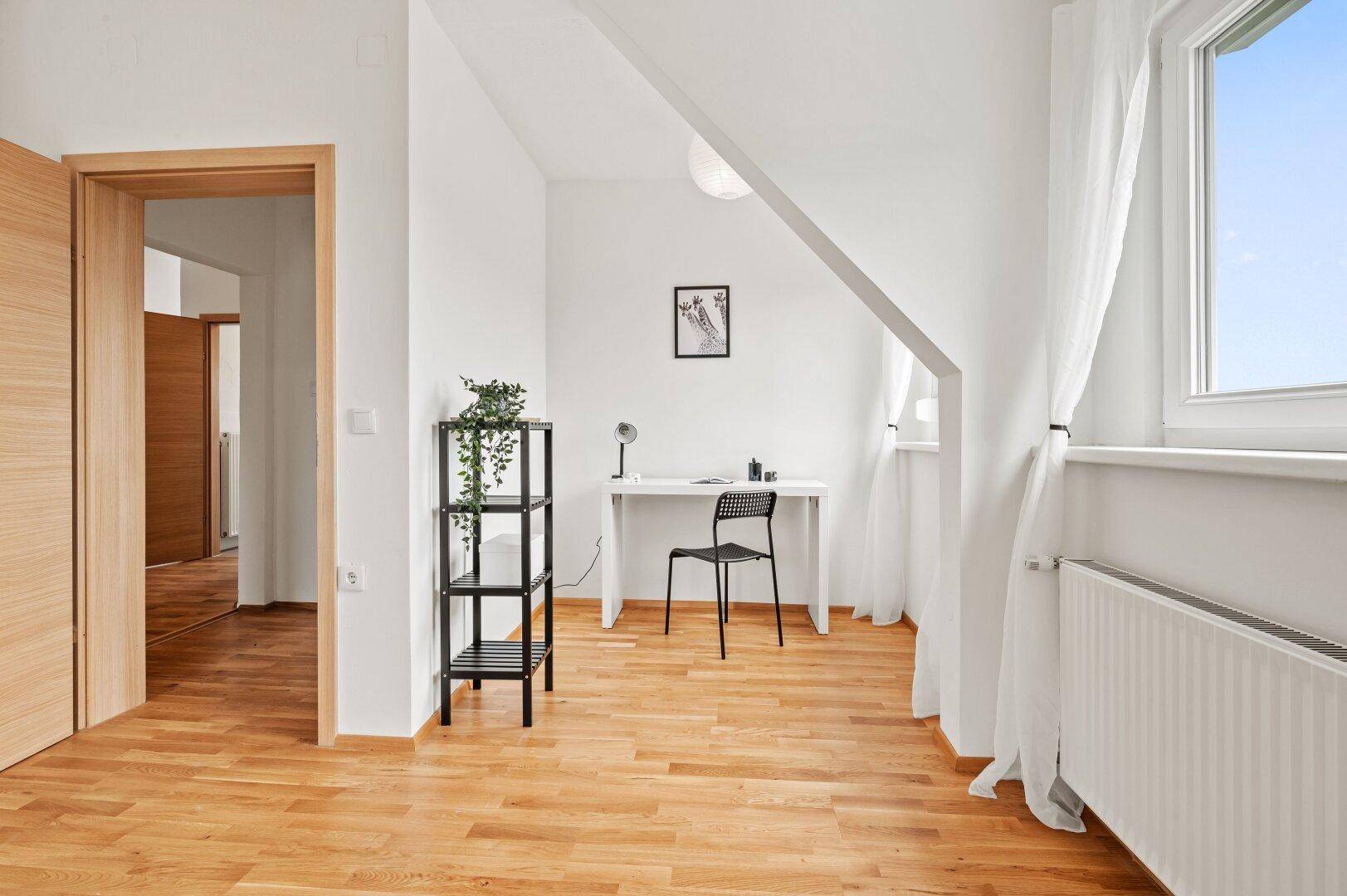 Helles Arbeitszimmer im Dachgeschoss mit Holzboden, Schreibtisch und Dachschräge.