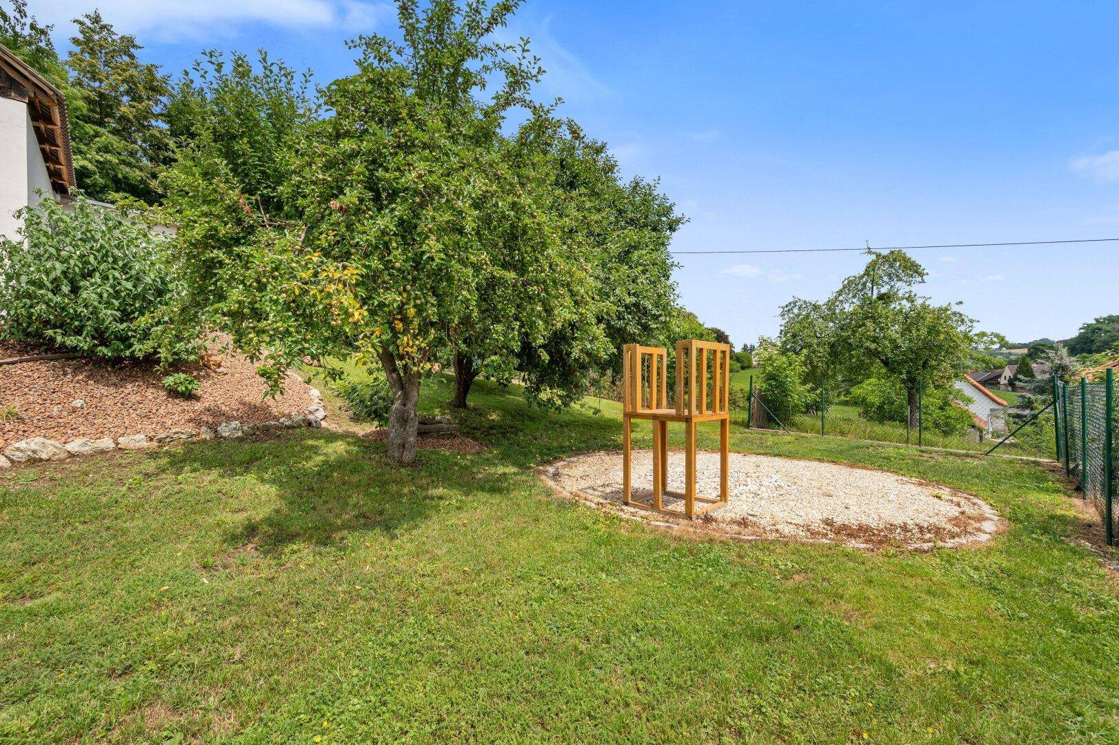 Grüner Gartenbereich mit Obstbäumen und einem kleinen Spielplatz für Kinder.
