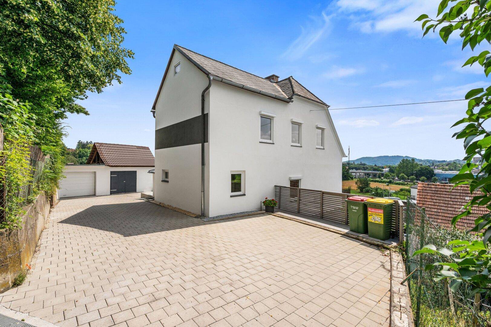 Seitenansicht des Hauses mit gepflasterter Zufahrt und Mülltonnenbereich.