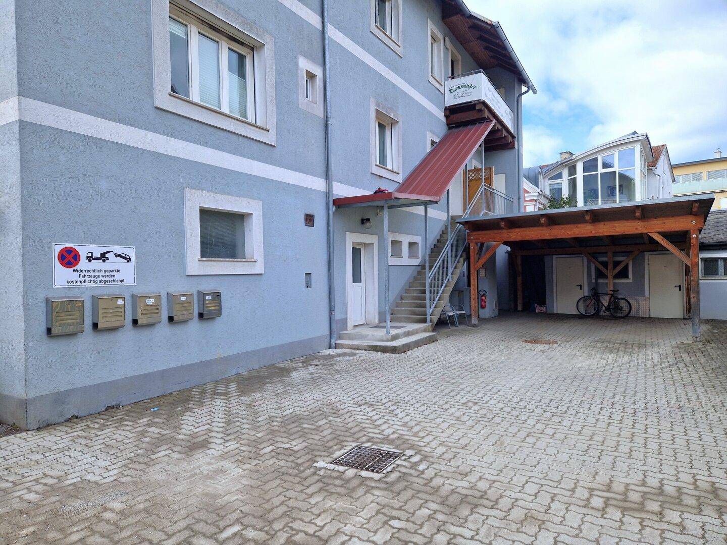 Eingangsbereich des Gebäudes mit Briefkästen, gepflastertem Vorplatz und Carport.