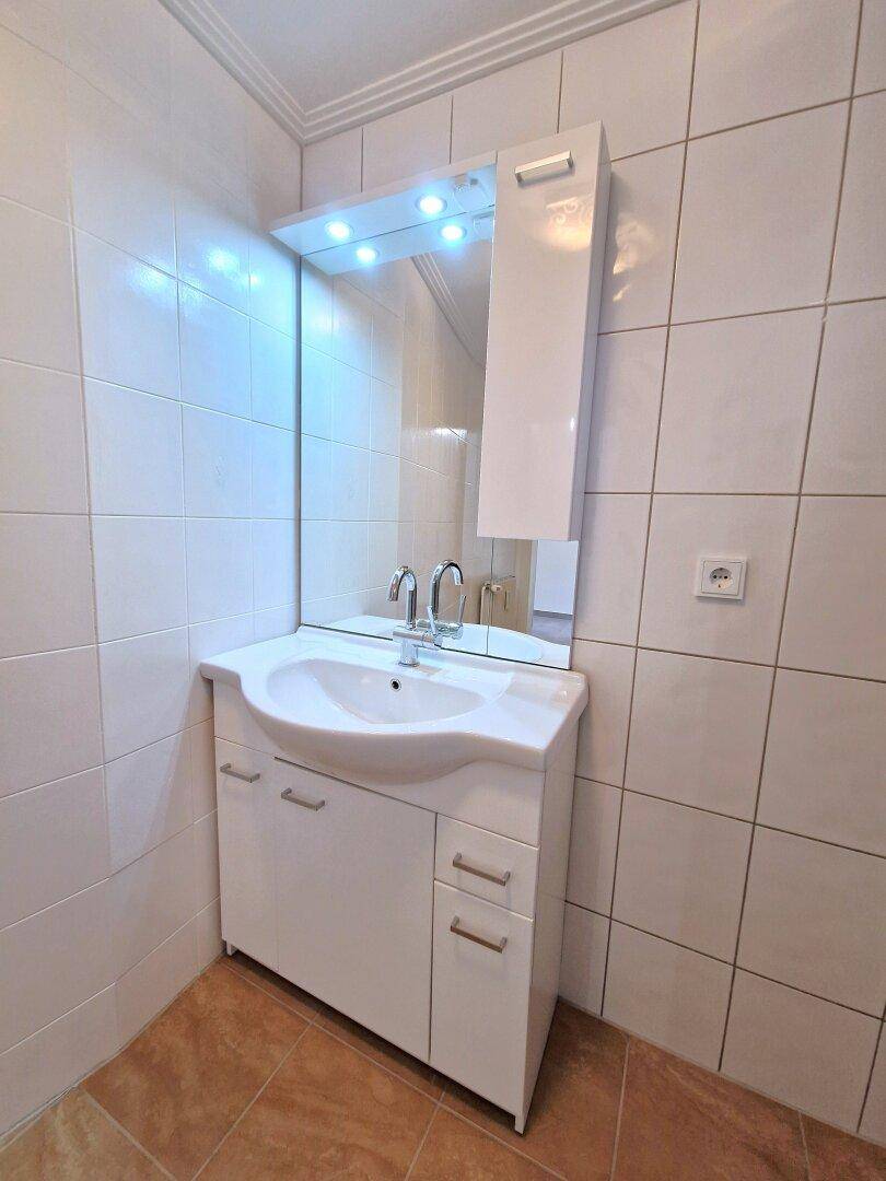 Badezimmer mit modernem Waschtisch, Spiegelschrank und weißen Wandfliesen.