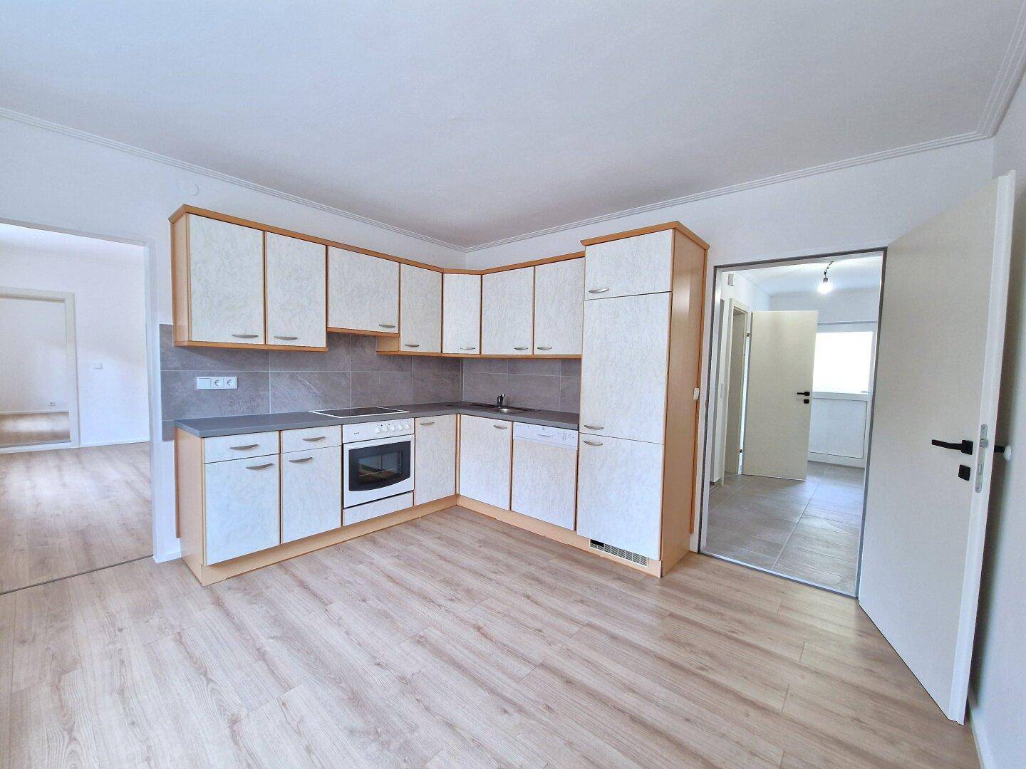 Geräumige Küche mit L-förmiger Einbauküche, Ofen und hellem Laminatboden.