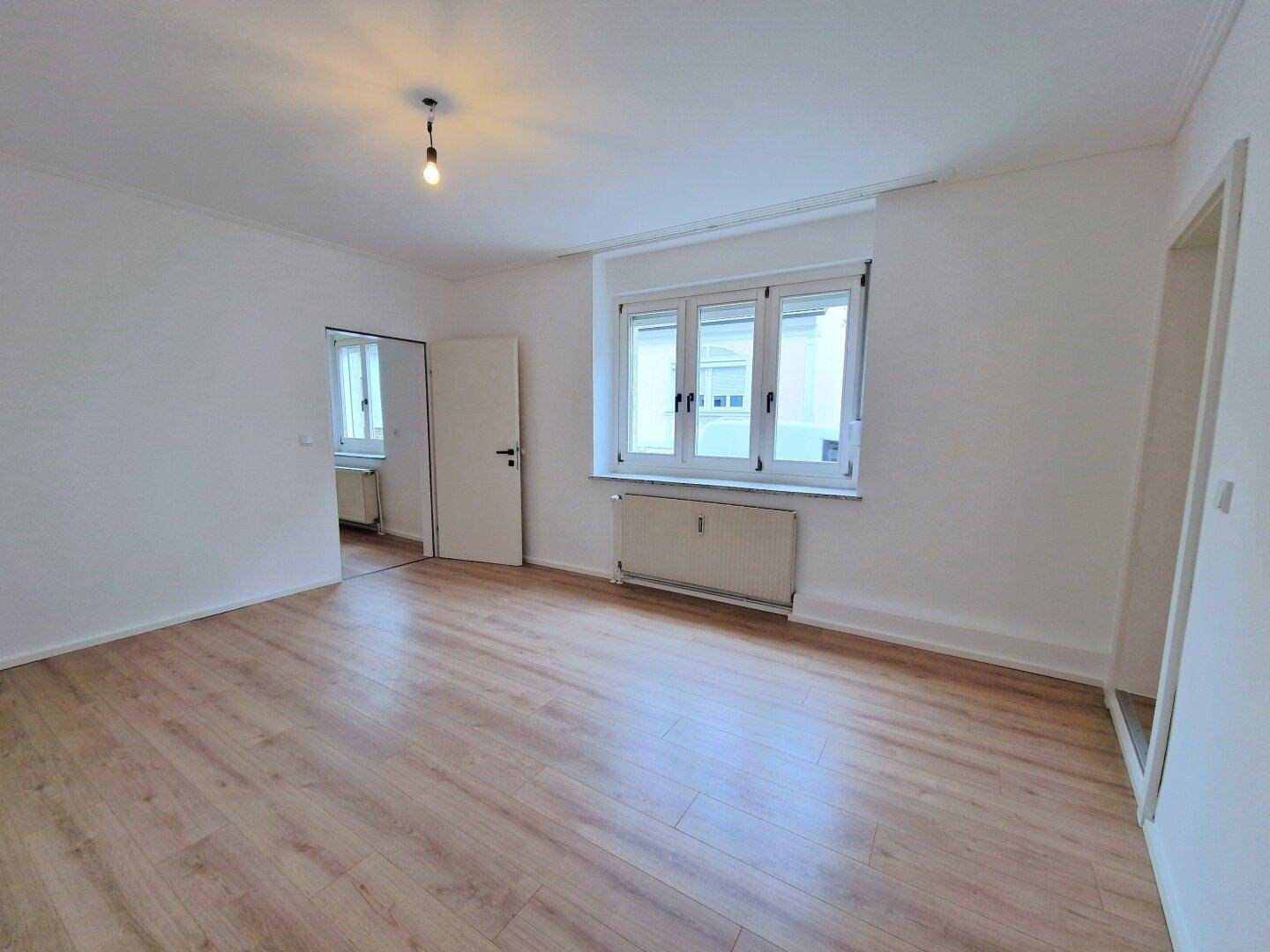 Heller, leerer Raum mit Laminatboden, Fenster und Heizkörper.