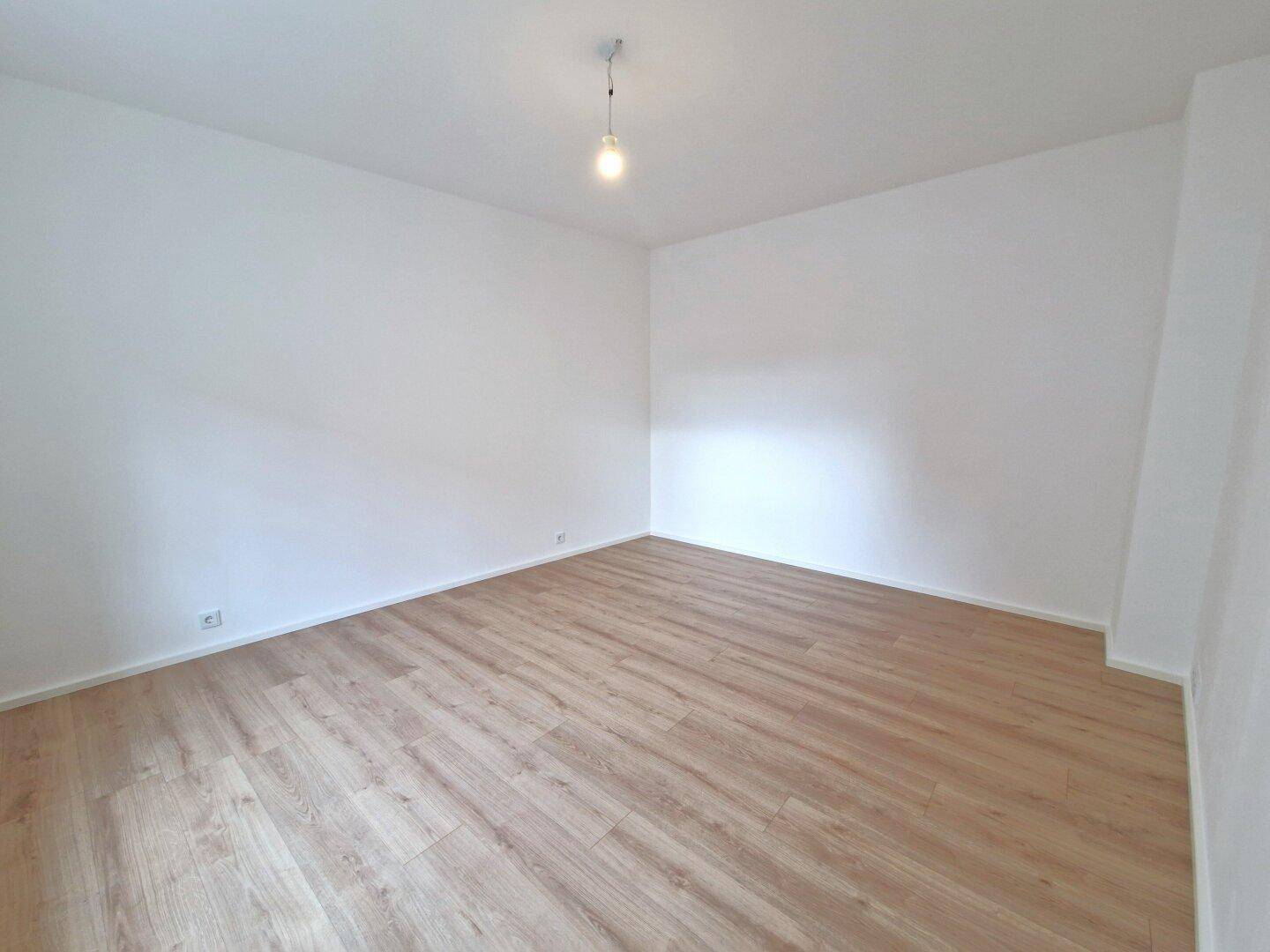 Leeres, helles Schlafzimmer mit Laminatboden und weißen Wänden.