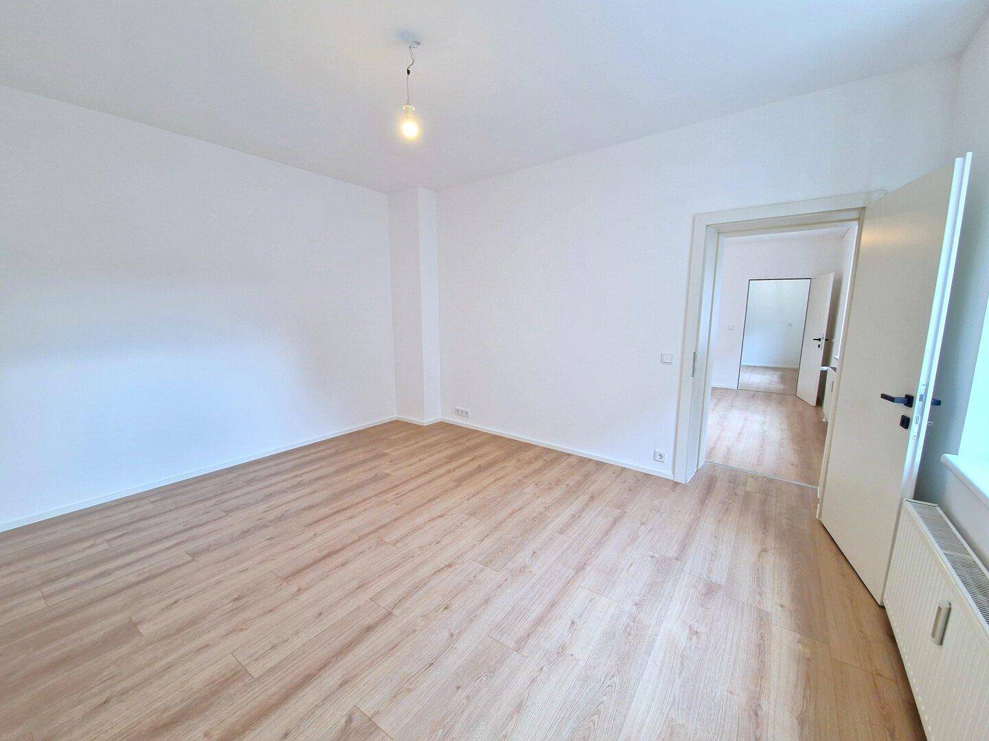 Heller, leerer Raum mit Laminatboden und Zugang zu einem weiteren Zimmer.