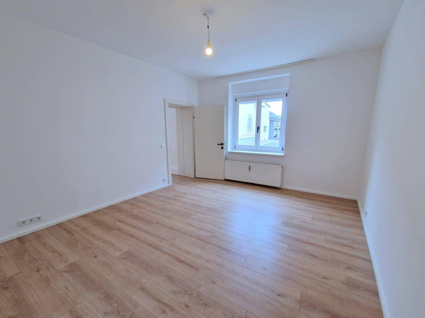 Heller, leerer Raum mit Laminatboden, Fenster und Heizkörper.