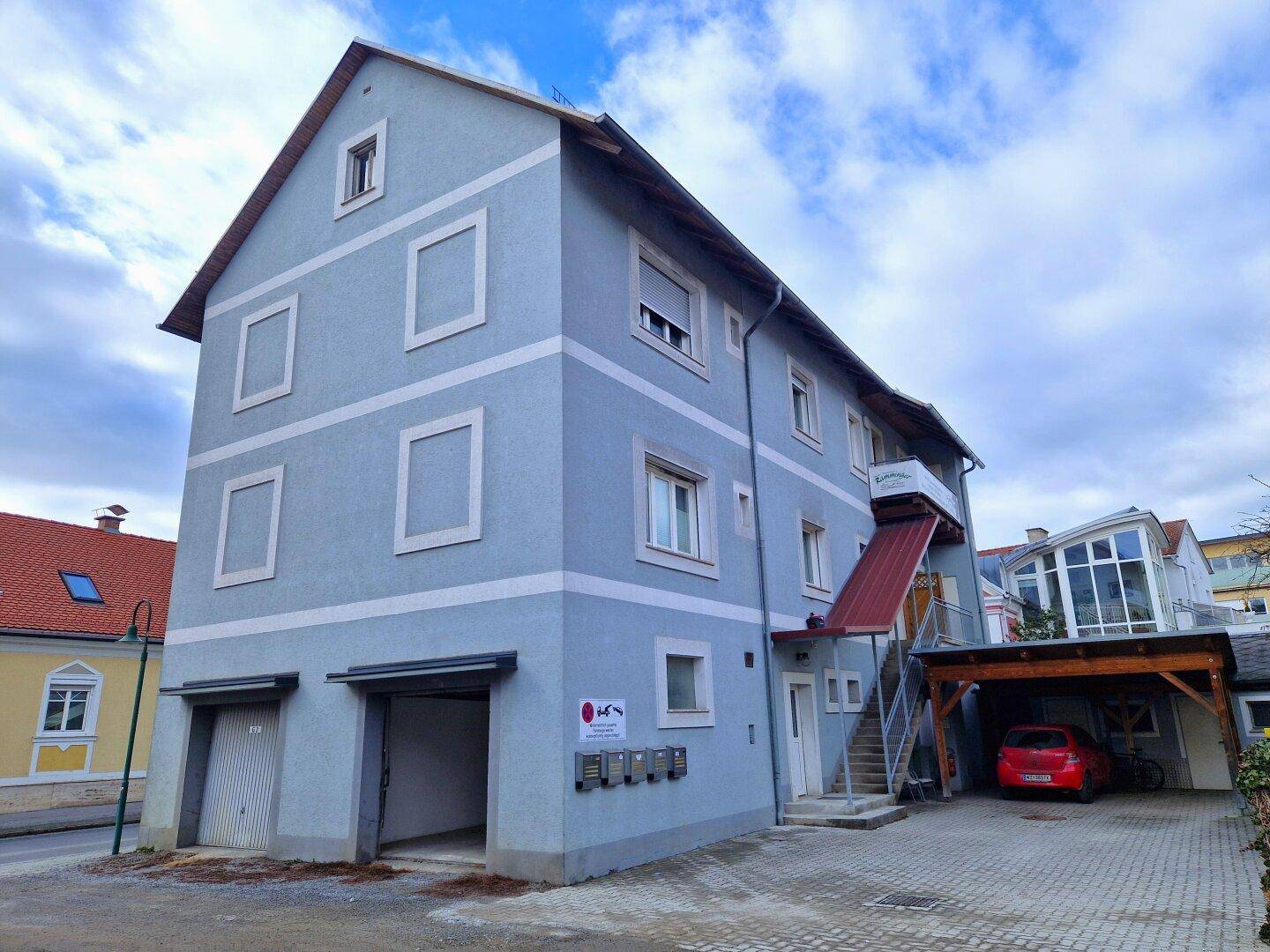 Mehrstöckiges Gebäude mit blauer Fassade, Carport und externer Treppe mit Rampe.