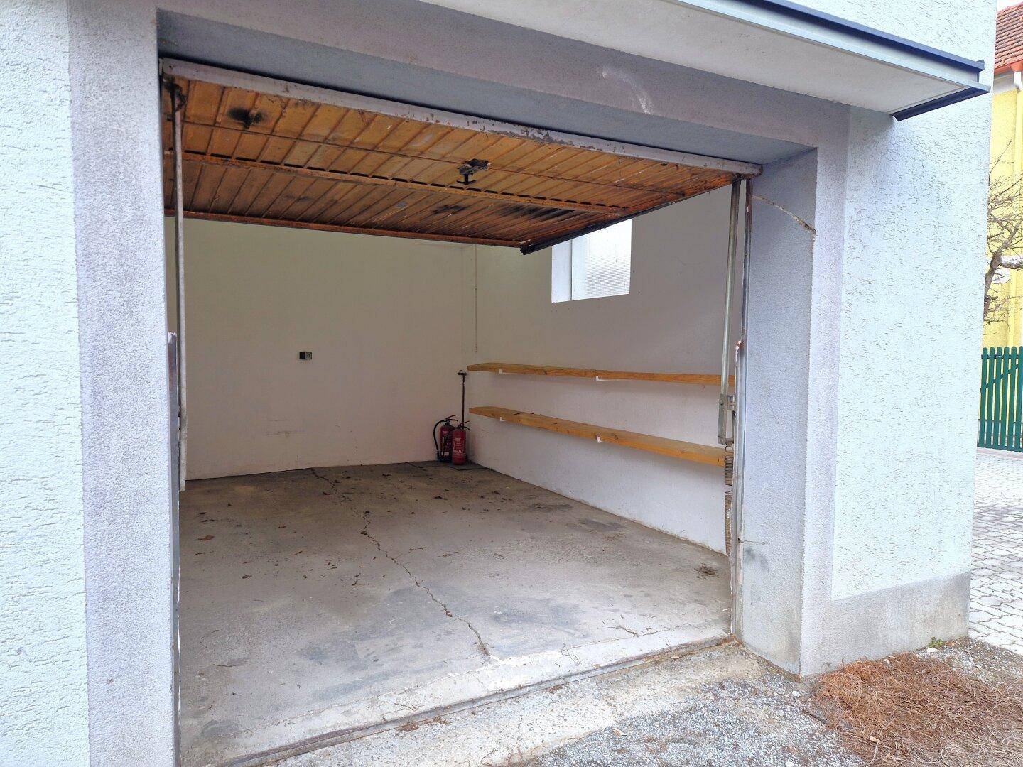 Leere Garage mit Betonboden, weißen Wänden und Holzdecke.
