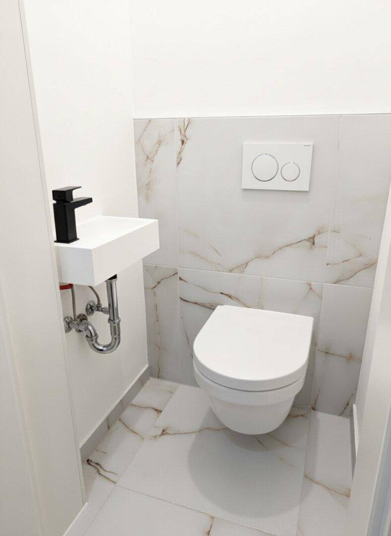 Modernes Gäste-WC mit wandhängender Toilette und kleinem Waschbecken, elegant gefliest.